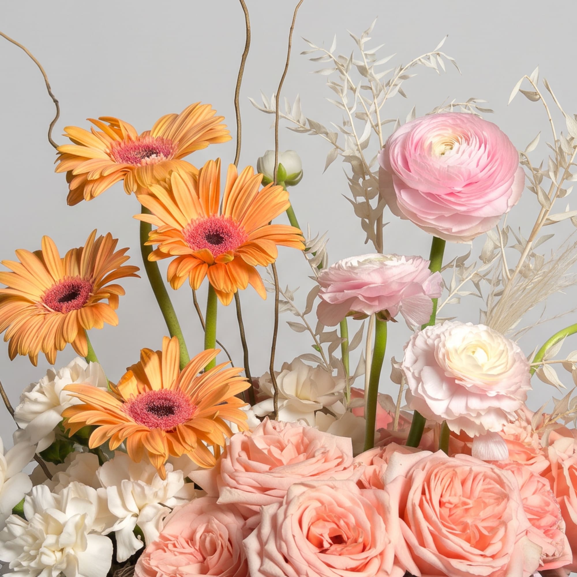 Pink and peach flowers arranged with orange daisies and pale filler blooms