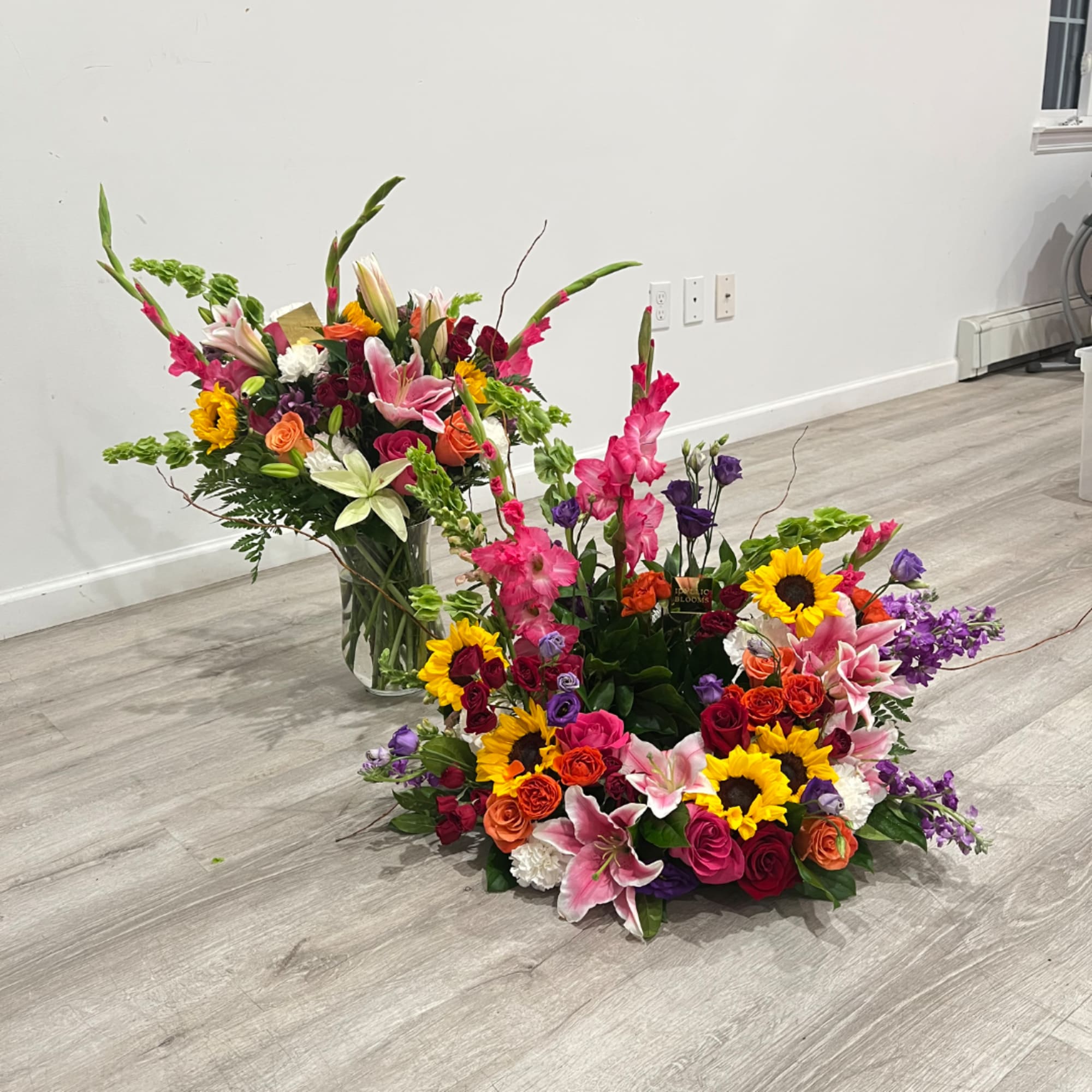 Two colorful floral arrangements with sunflowers, roses, and lilies on the floor