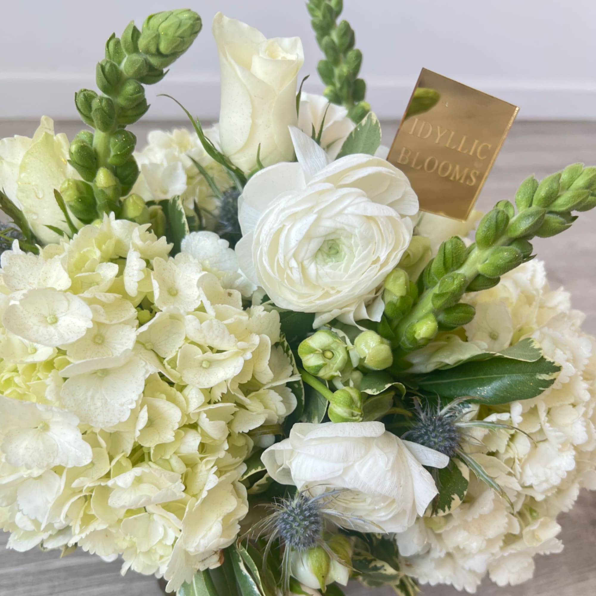 White floral arrangement with hydrangeas, roses, and green spires in a vase