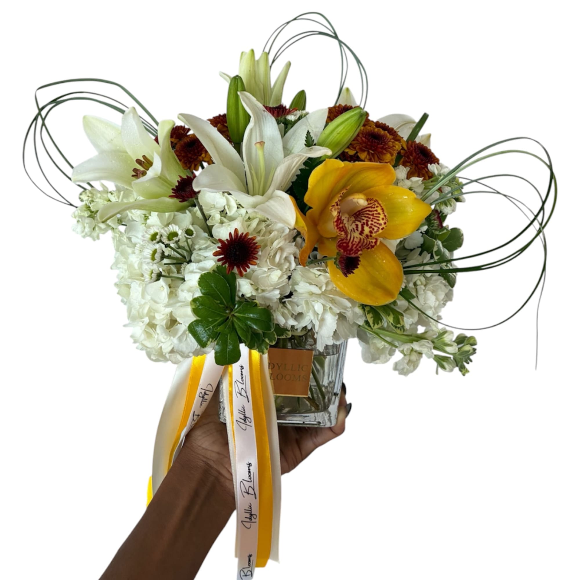White and yellow floral arrangement in a glass vase with ribbon tails
