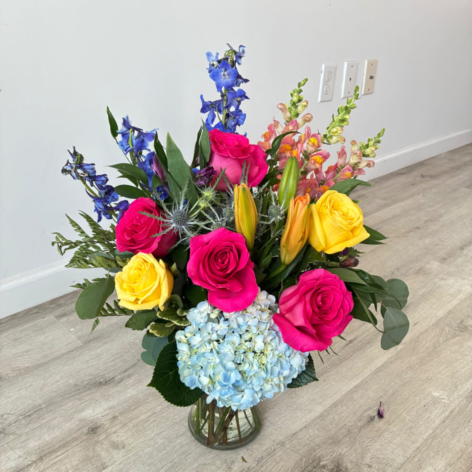 Mixed bouquet in a glass vase with roses, hydrangea, lilies, and blue delphinium
