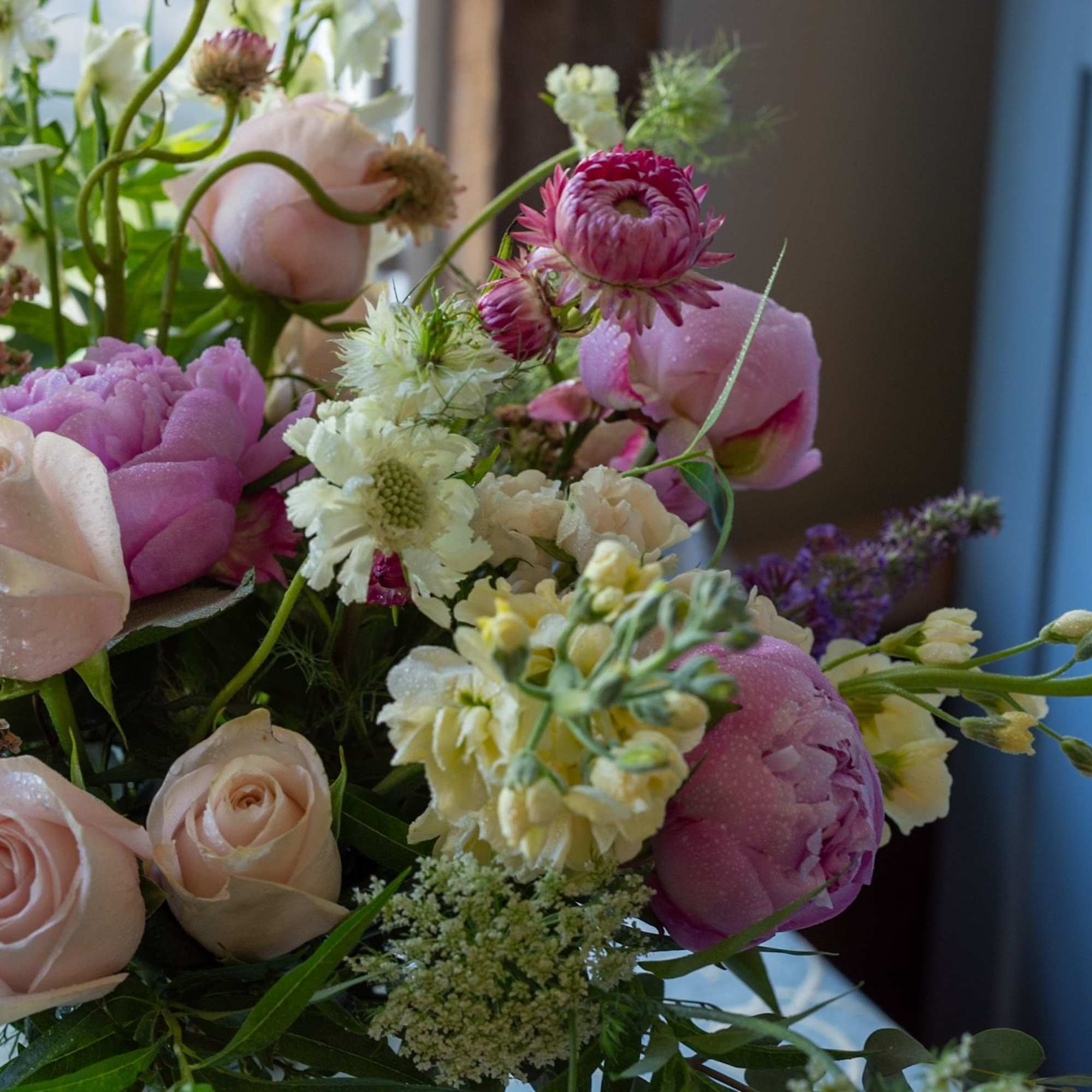 Pastel arrangement of pink roses, peonies, and cream blossoms in a loose garden-style bouquet