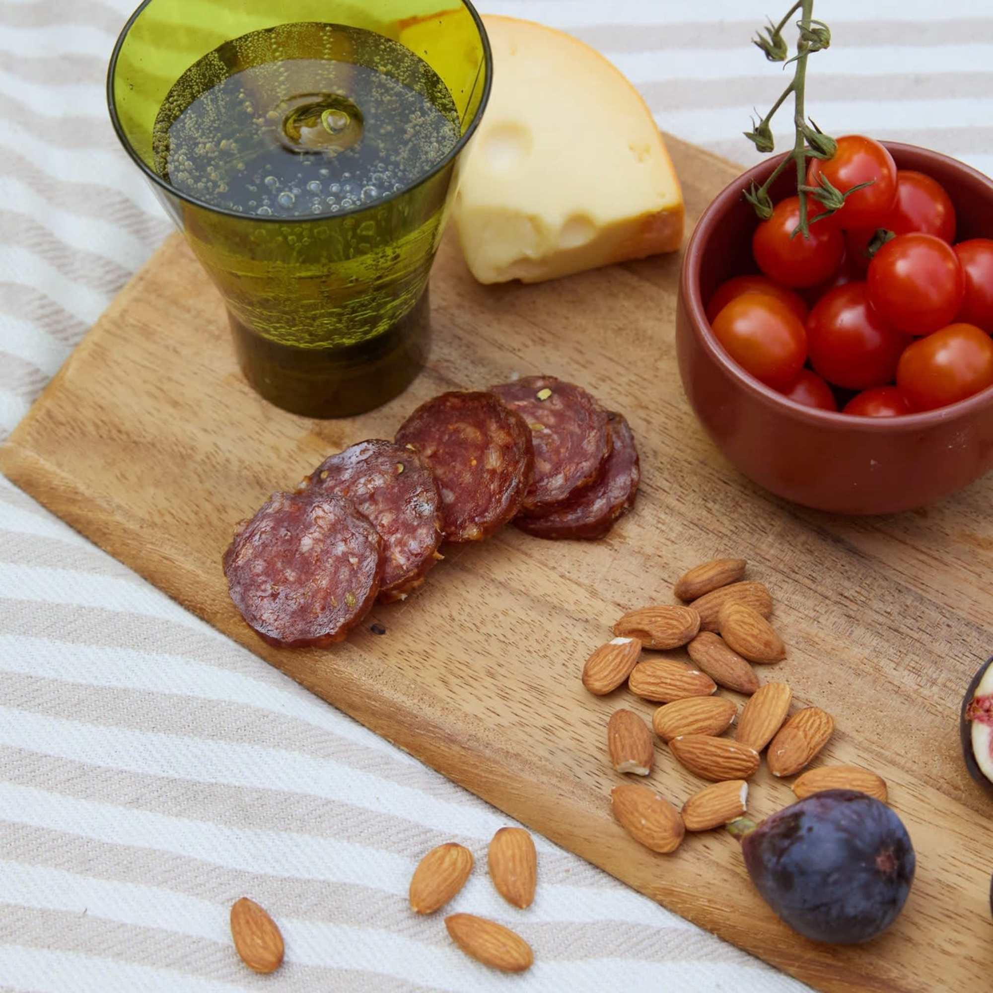 Charcuterie board with wine, cheese, salami, tomatoes, almonds, and a fig
