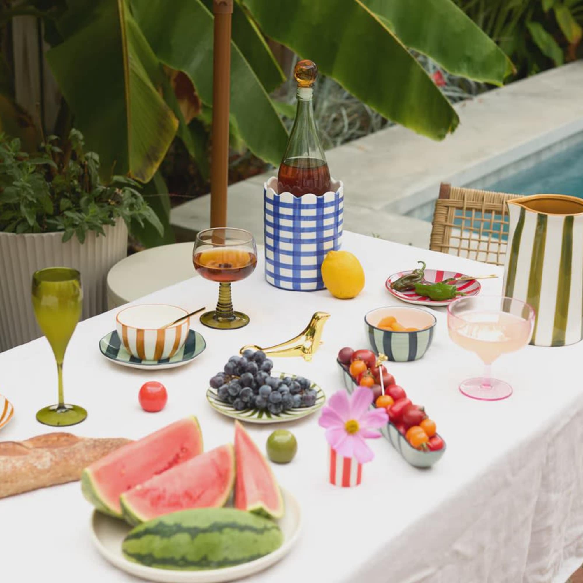 Outdoor table with fruit, drinks, and a small pink flower in a striped vase