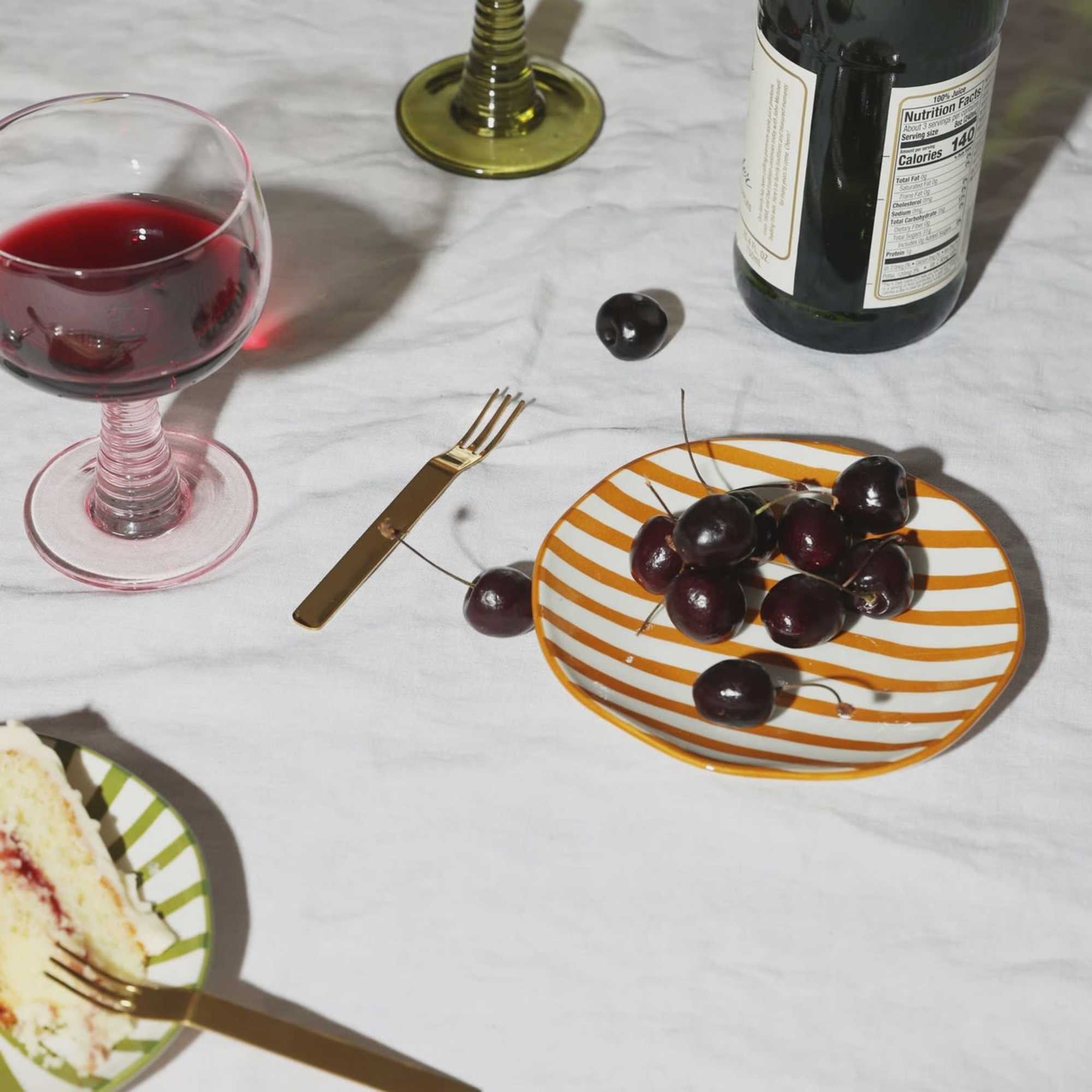 Wine glasses and a bottle beside cherries on striped plates