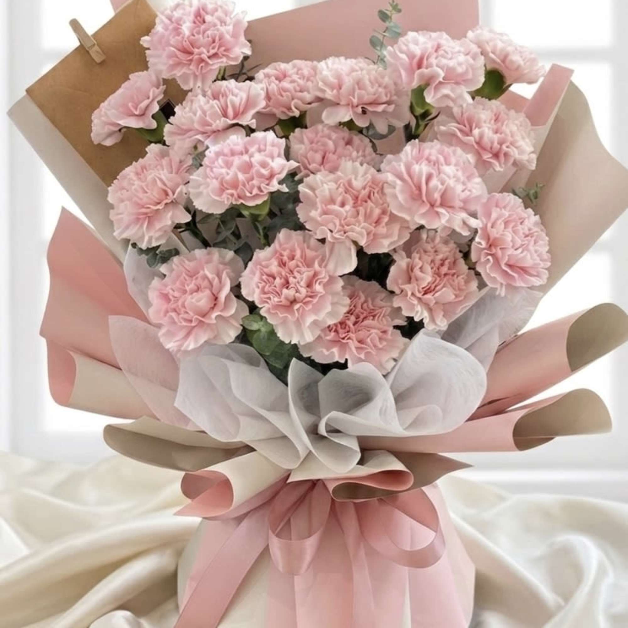 Bouquet of pale pink carnations wrapped in pink and beige paper