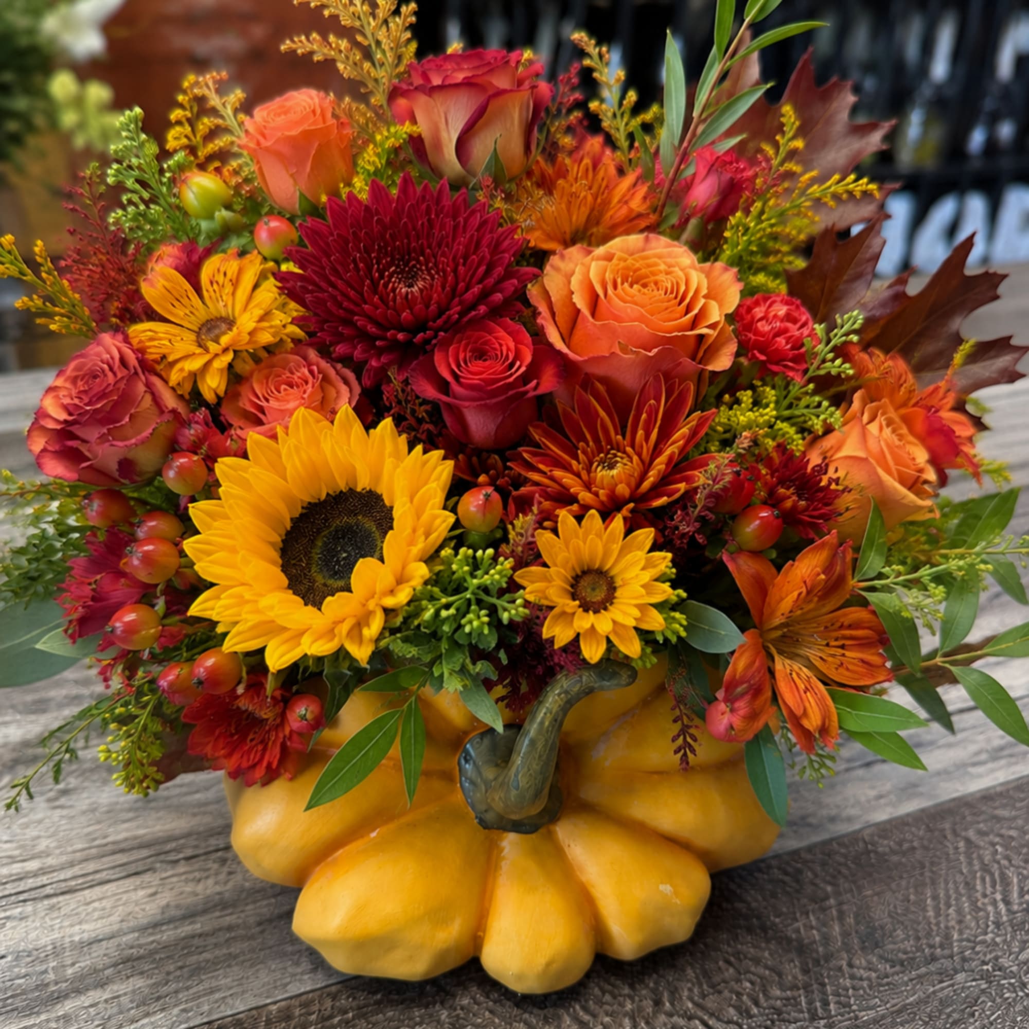 Autumn bouquet in a yellow pumpkin container with sunflowers, roses, and chrysanthemums