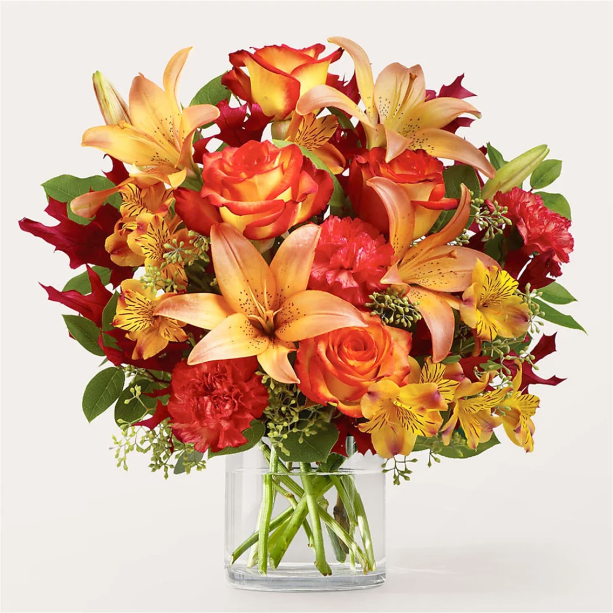 Bouquet of orange roses, lilies, and red carnations in a clear glass vase
