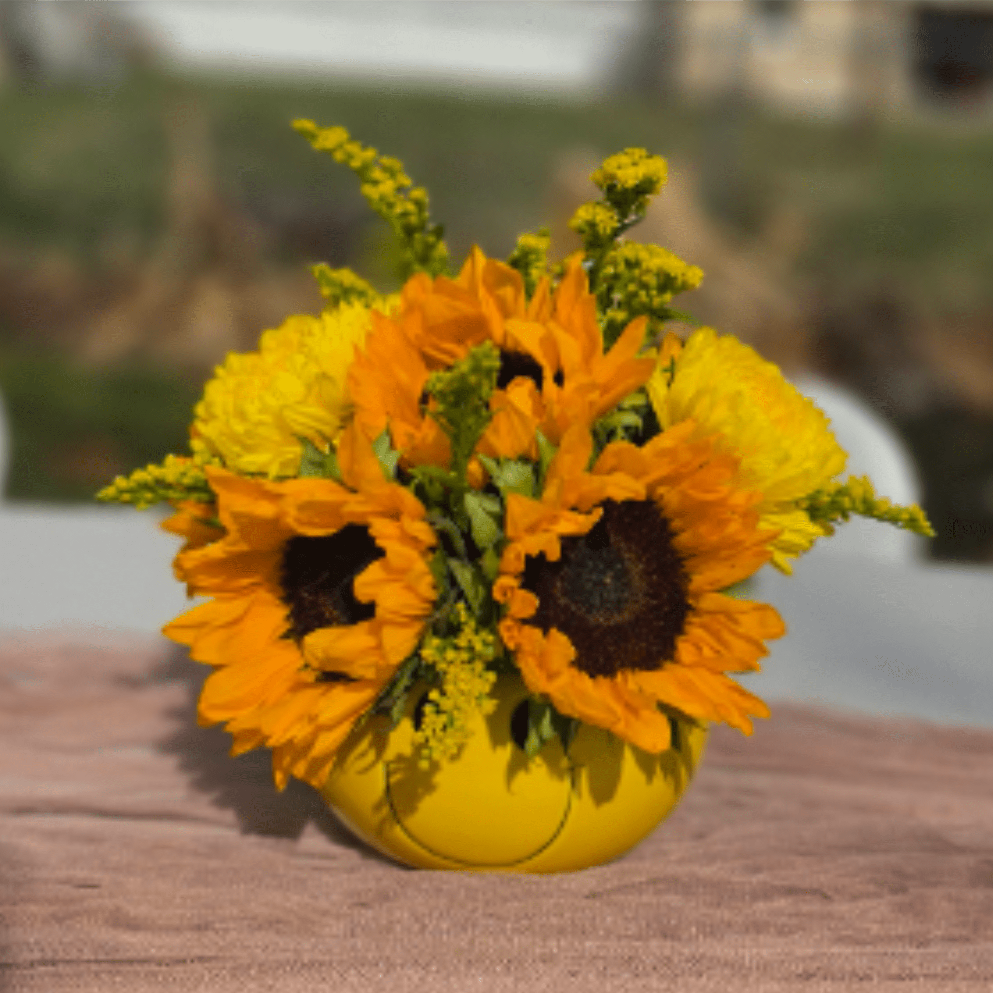 Compact arrangement of bright sunflowers and yellow blooms in a round yellow vase