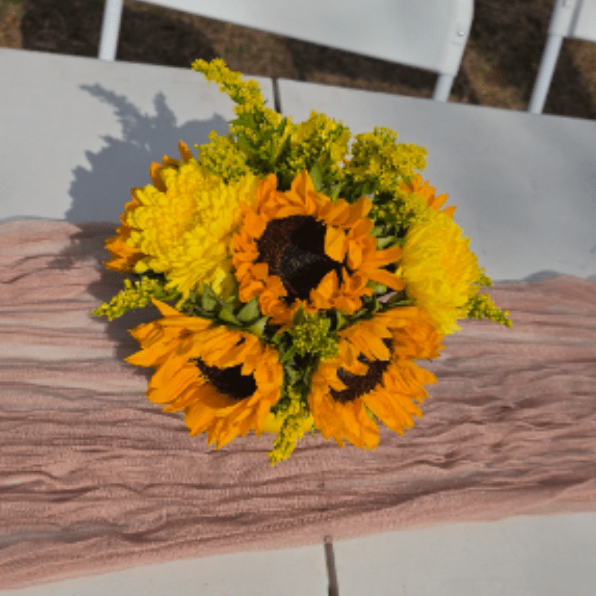 Compact bouquet of orange sunflowers and yellow flowers resting on a blush table runner.