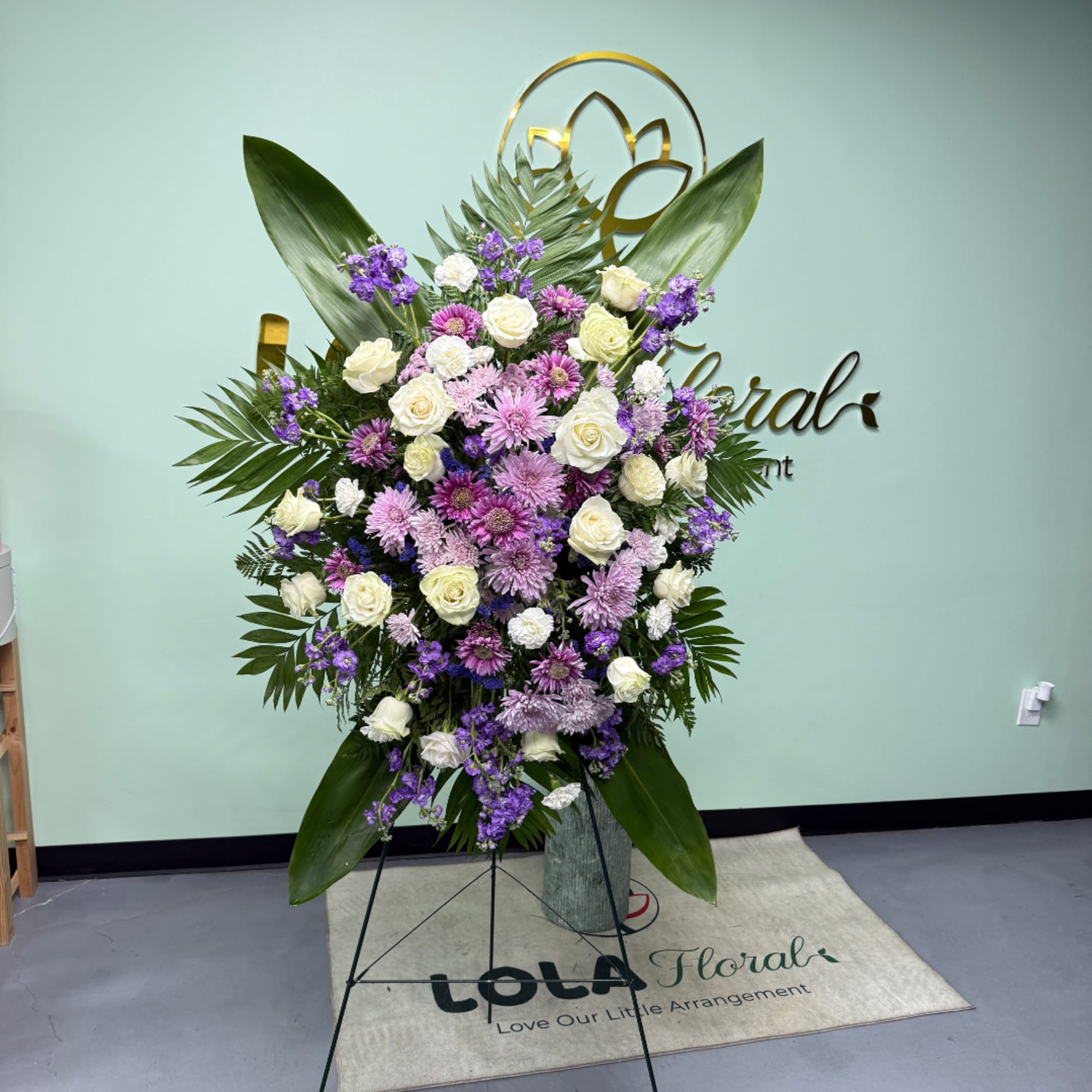 Large standing floral arrangement with white and purple flowers on an easel