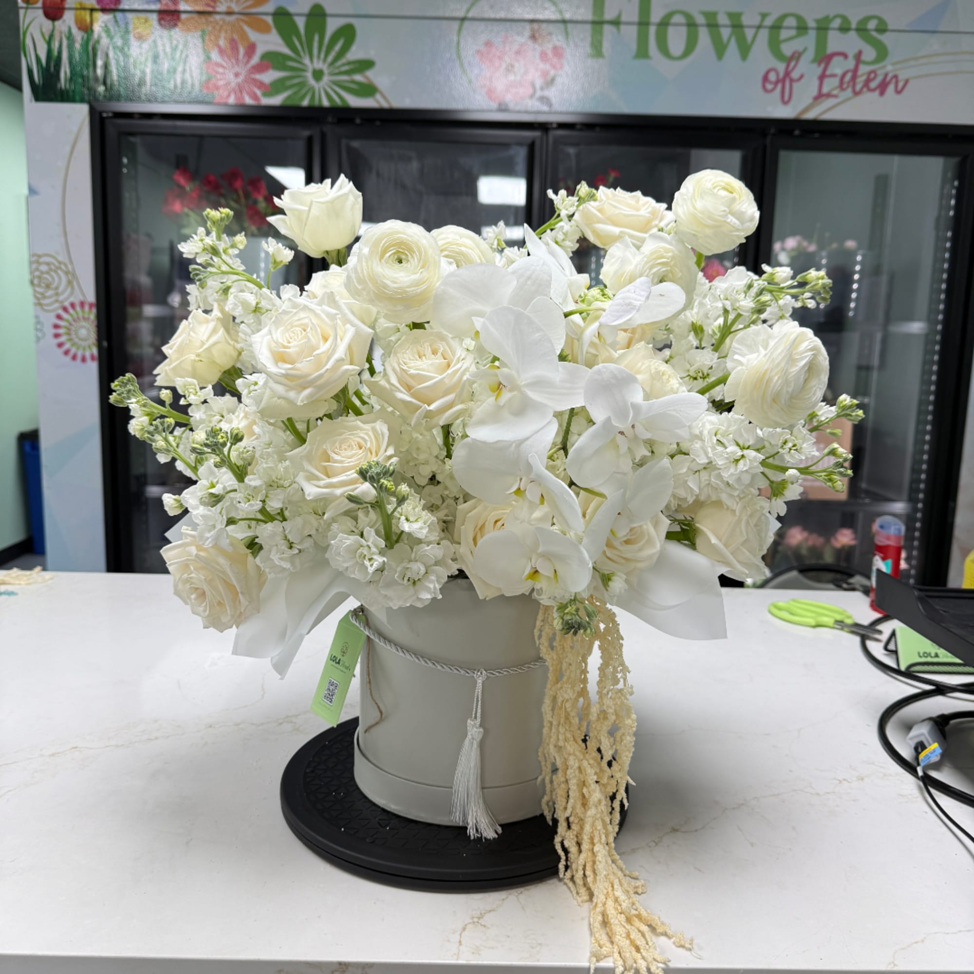 White roses and orchids arranged in a round hatbox-style container