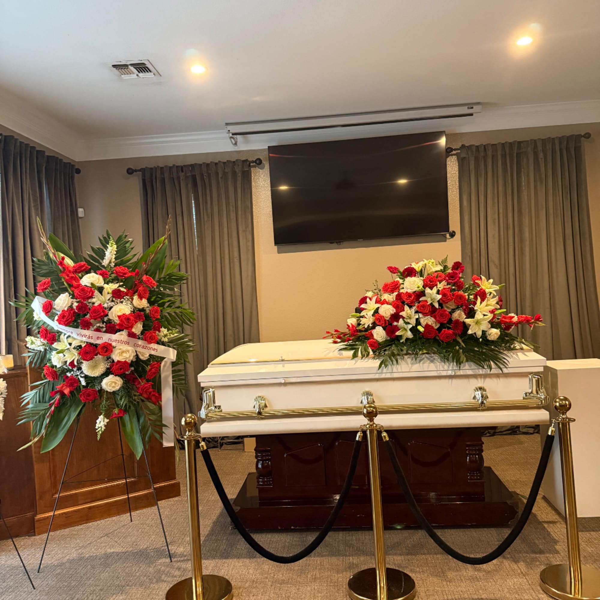 White casket with red and white floral sprays in a funeral room