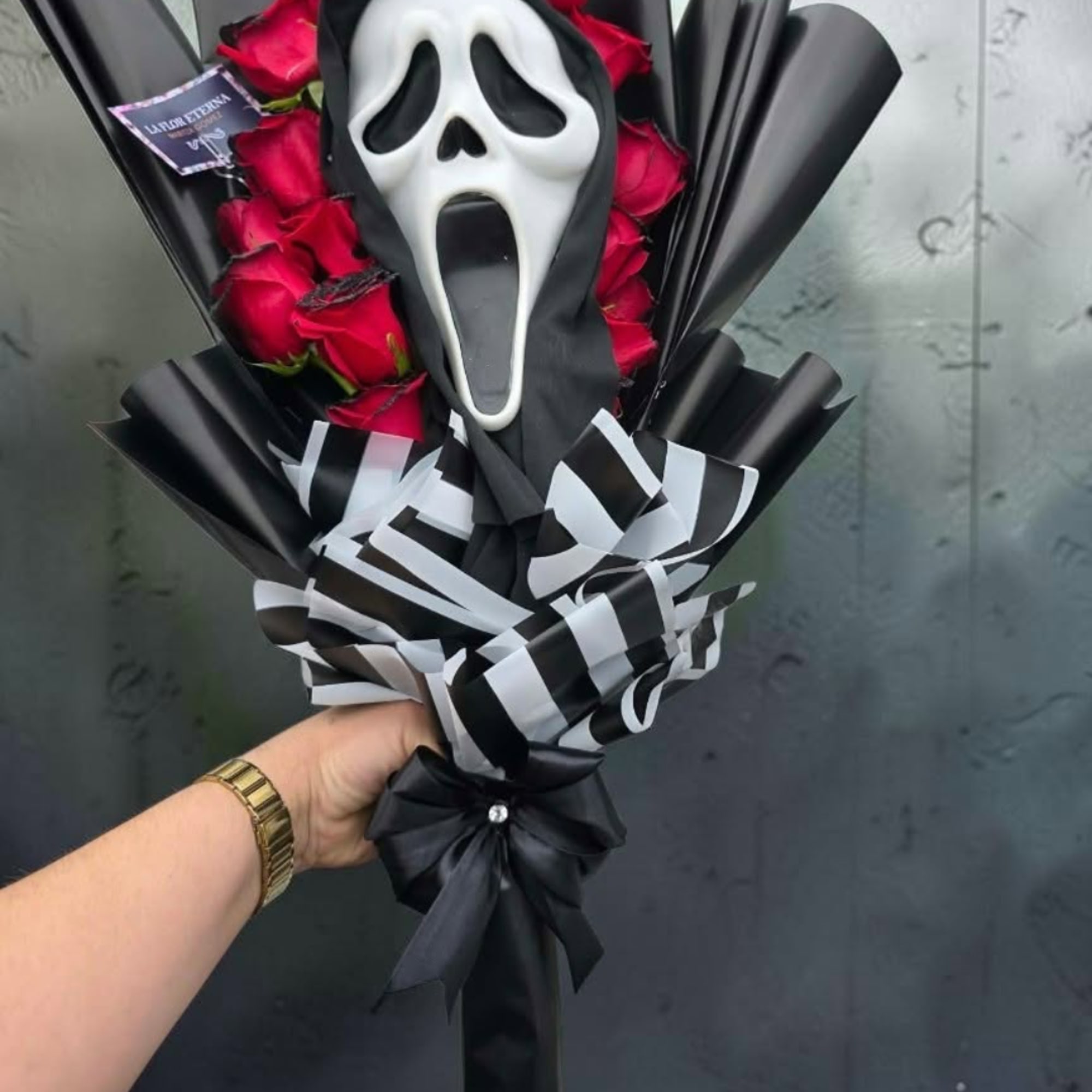 Bouquet of red roses wrapped in black paper with a Ghostface mask decoration