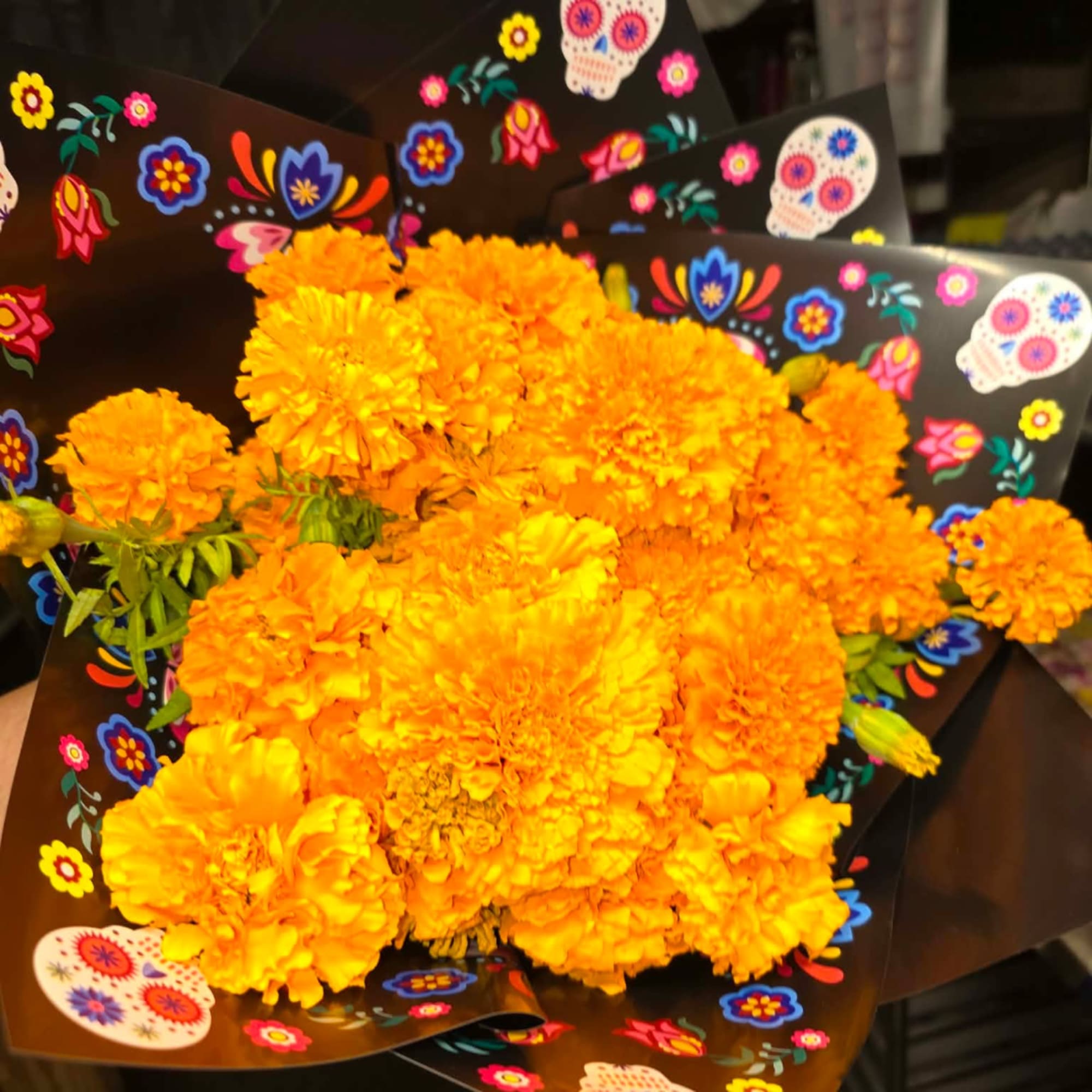Bouquet of bright orange marigolds wrapped in black paper with colorful skull patterns.