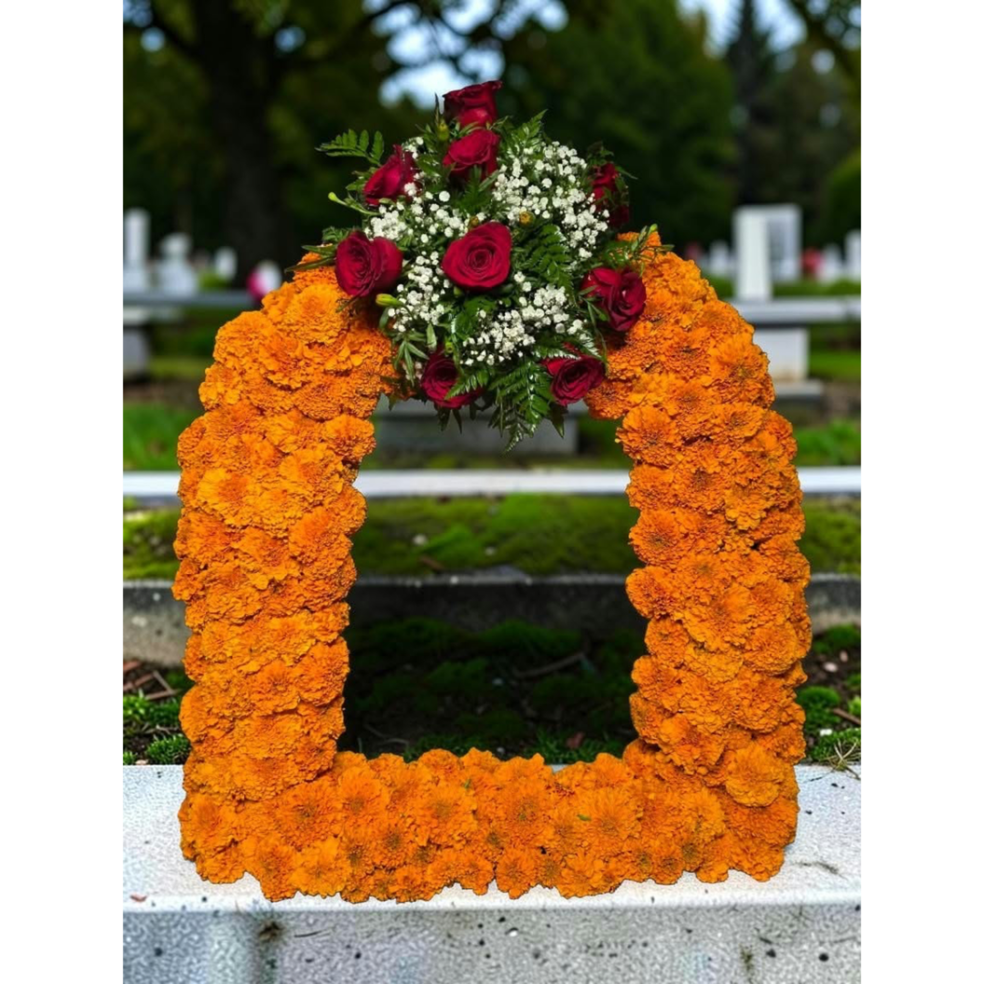Orange marigold funeral wreath with red roses and white filler flowers