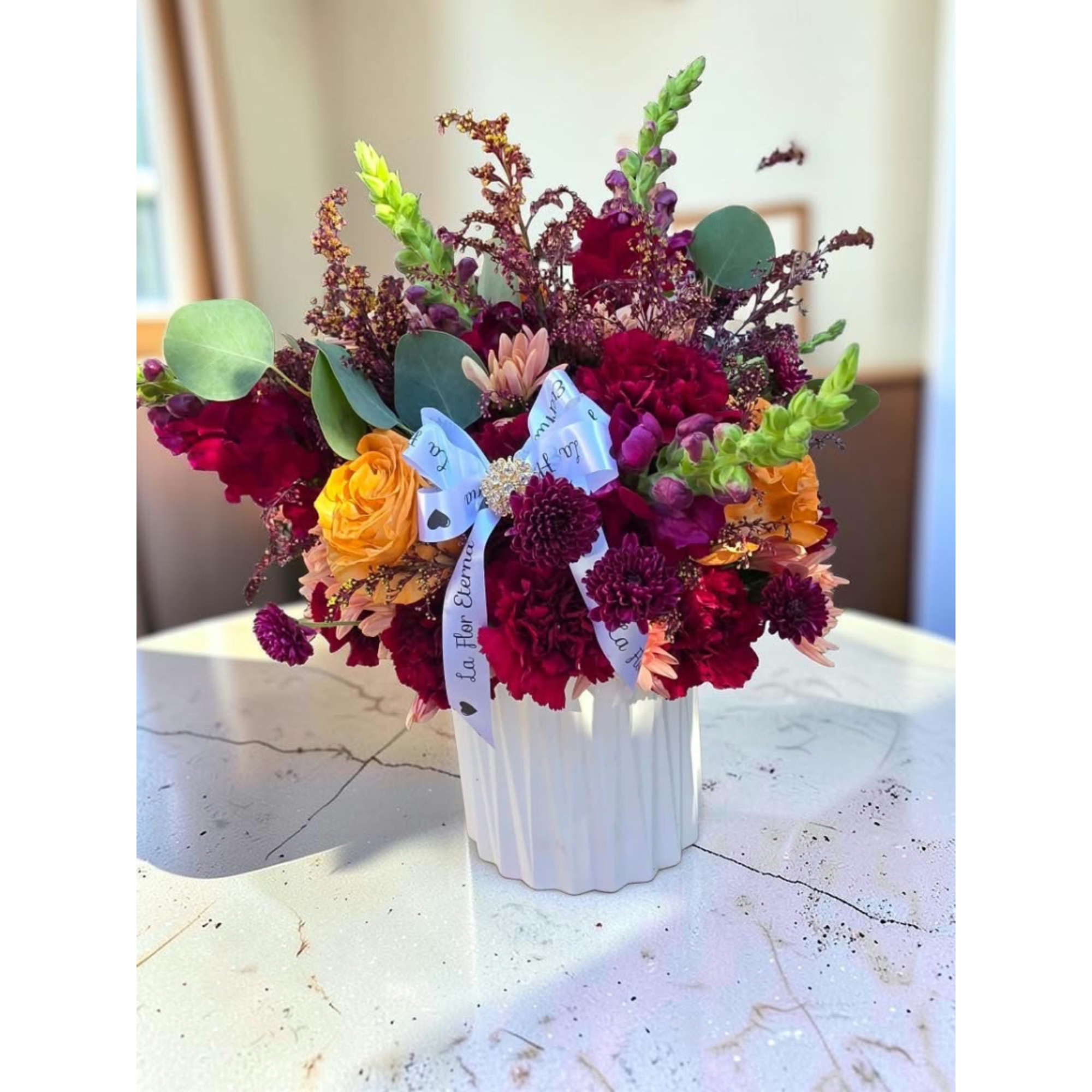 Mixed bouquet in a white ribbed vase with red, yellow, and purple flowers