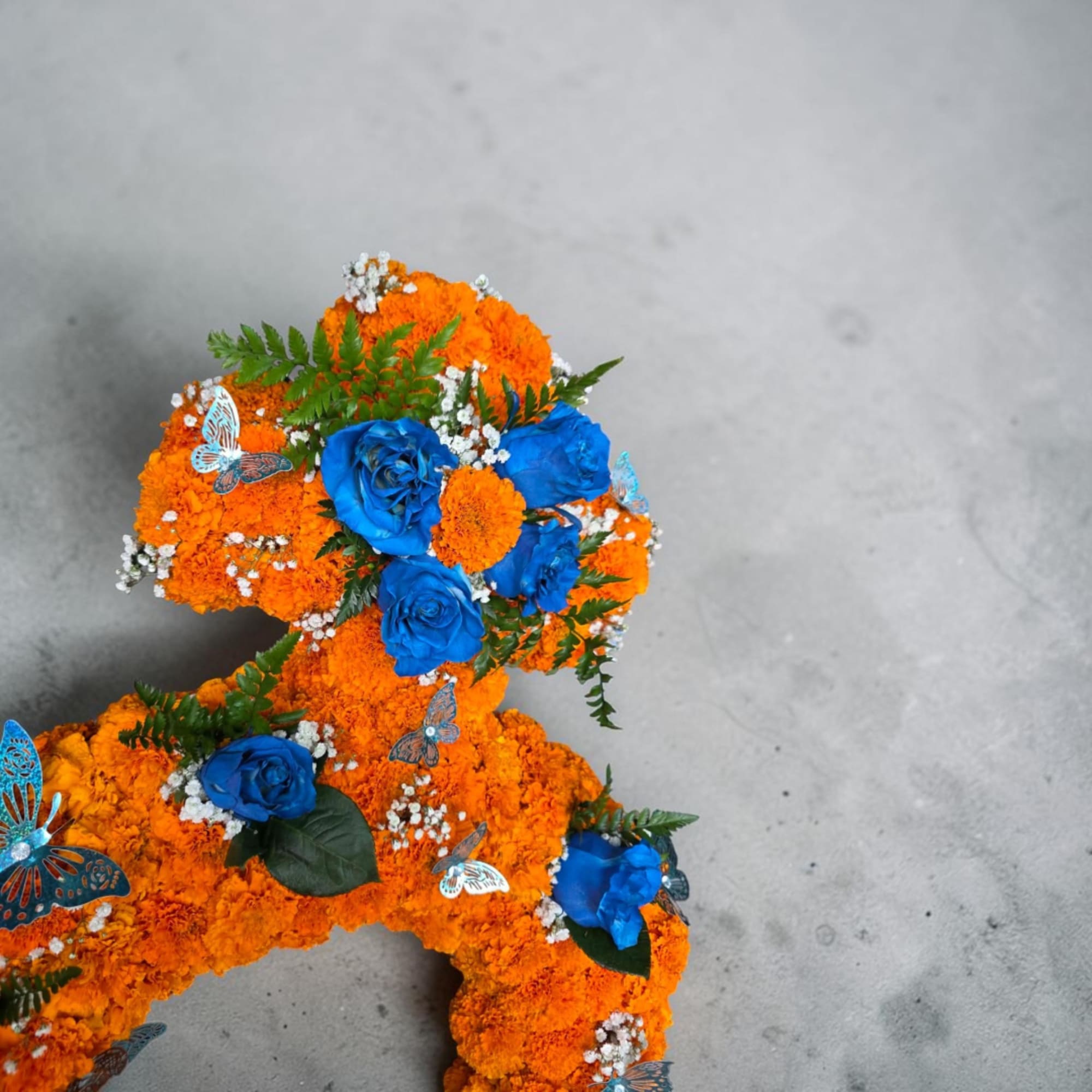 Orange marigold floral arrangement with blue roses and butterfly accents