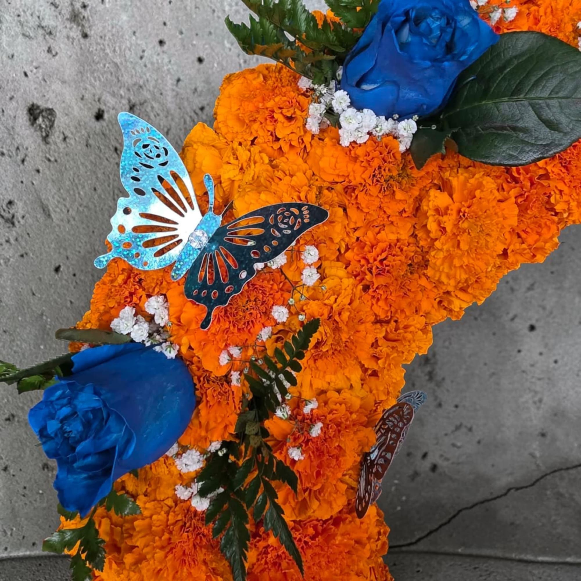 Orange marigold arrangement with blue roses and butterfly accents