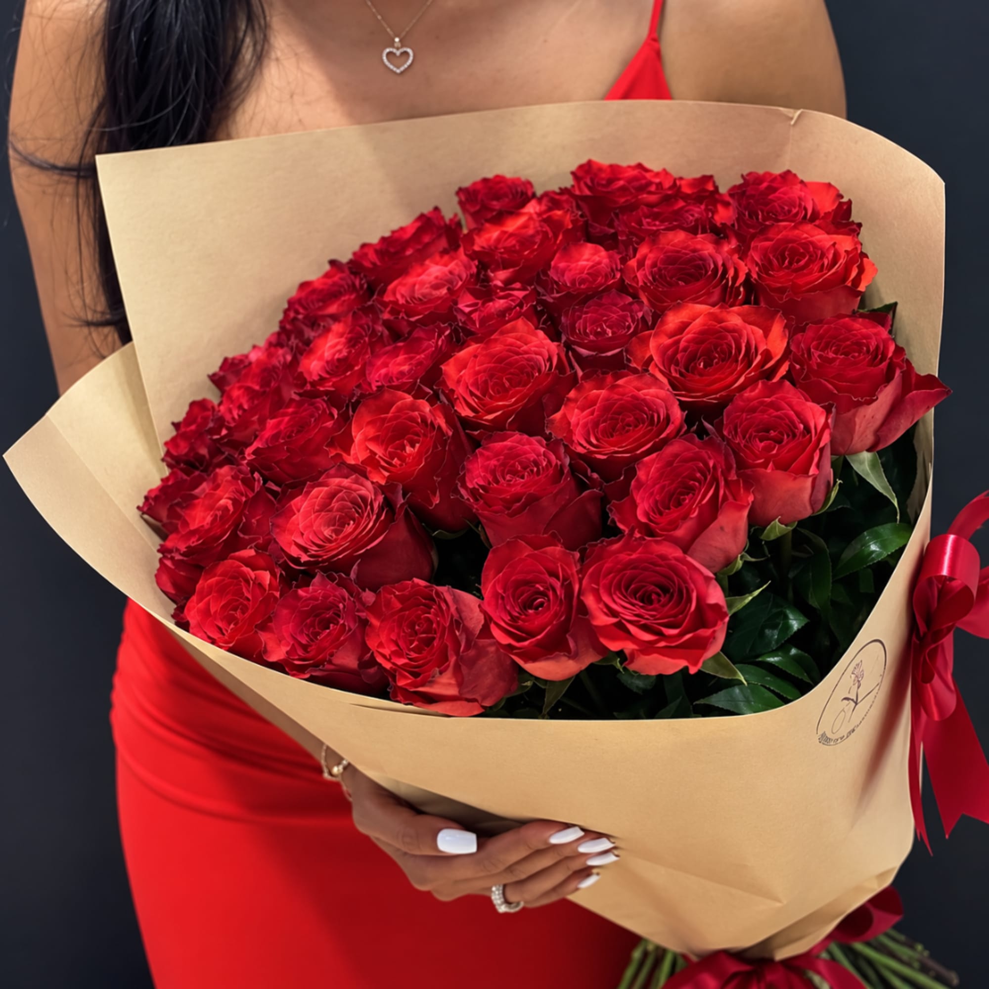 Large bouquet of red roses wrapped in tan paper with a red ribbon