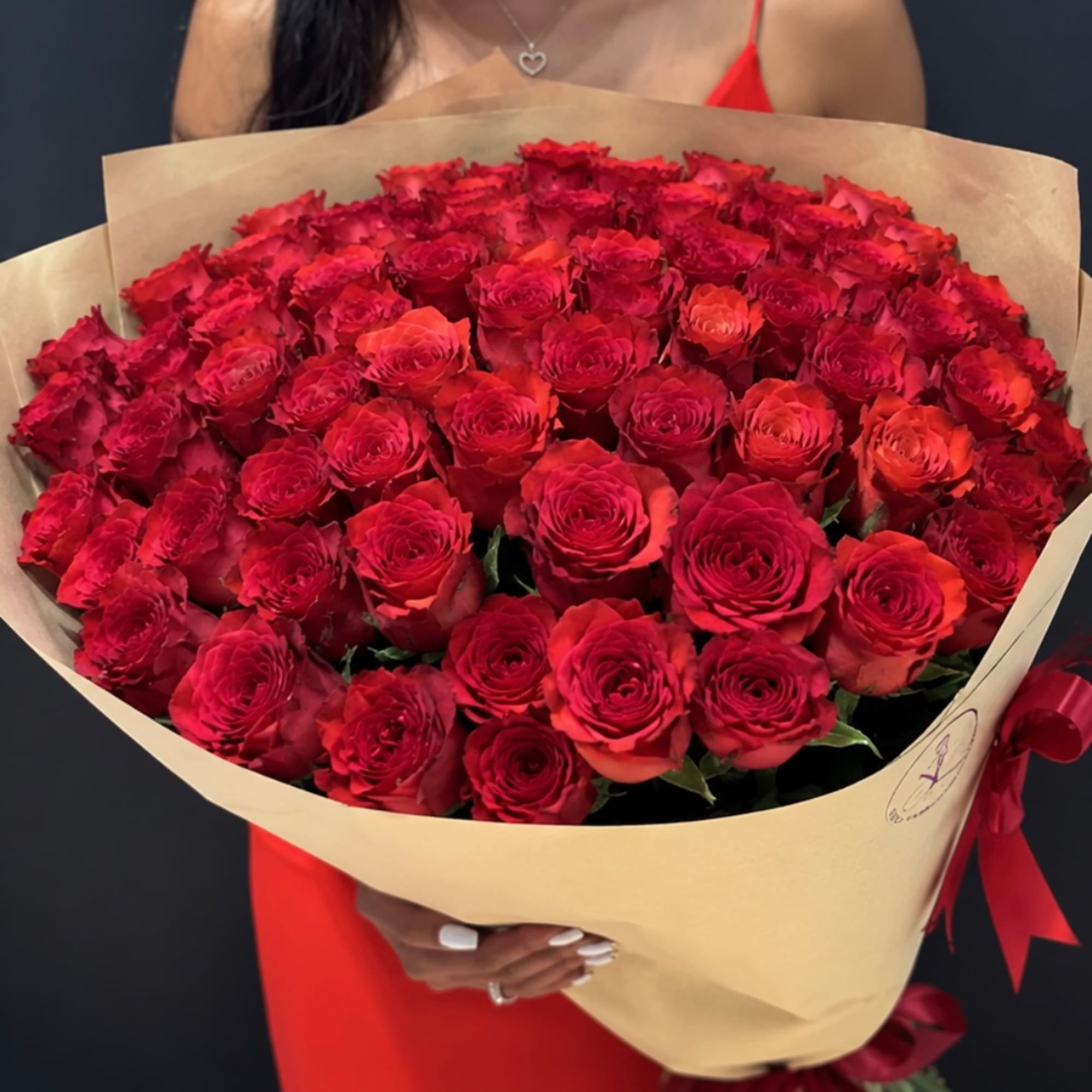 Large bouquet of red roses wrapped in tan paper with a red ribbon