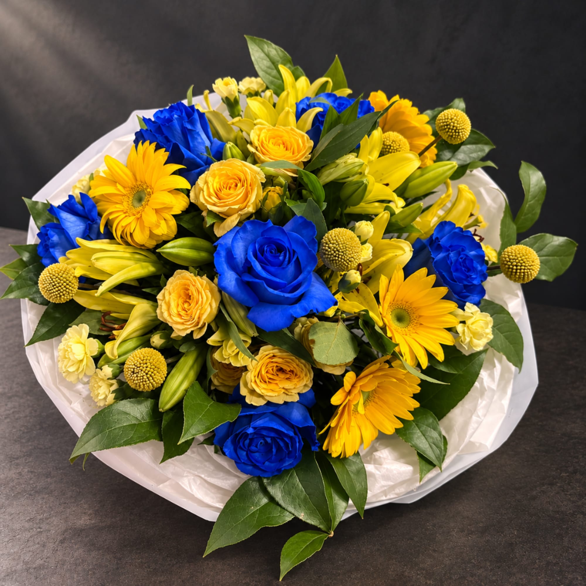 Bouquet of blue roses, yellow lilies, and yellow daisies in white wrap