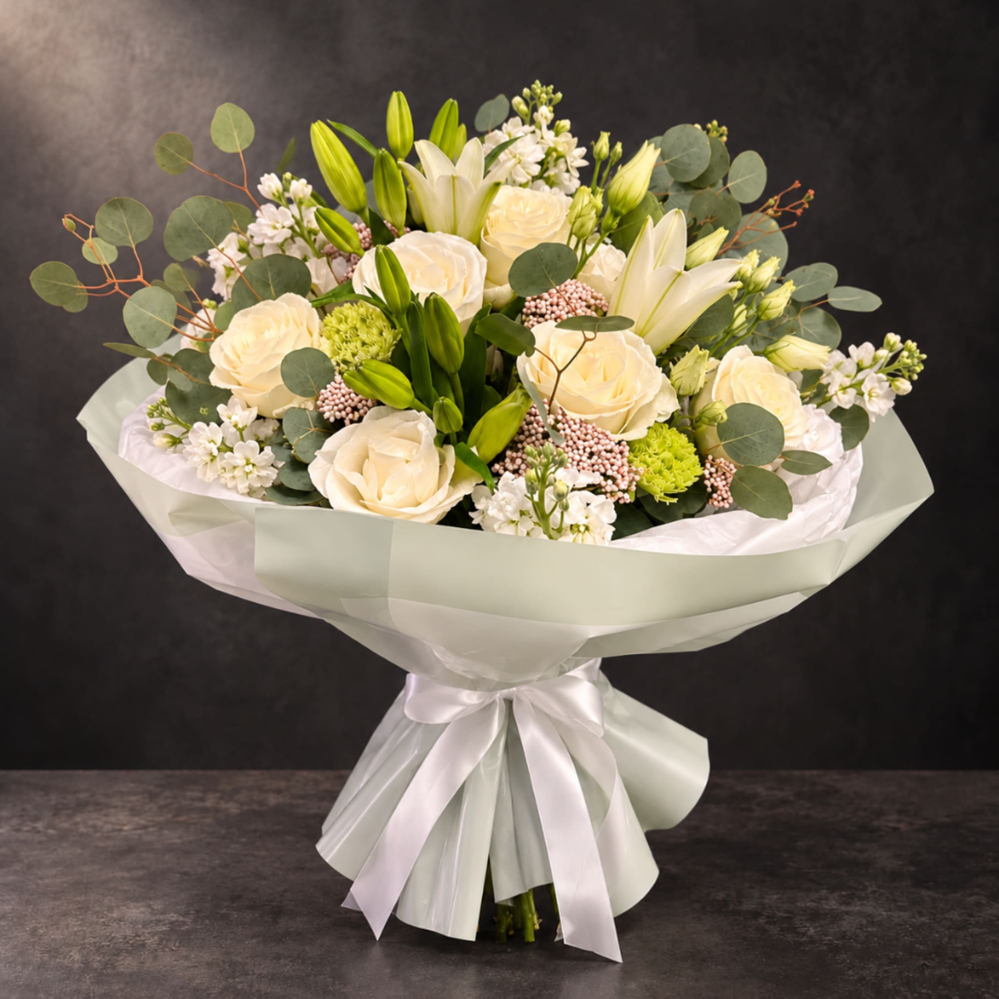 Bouquet of cream roses and white lilies wrapped in pale paper with a ribbon