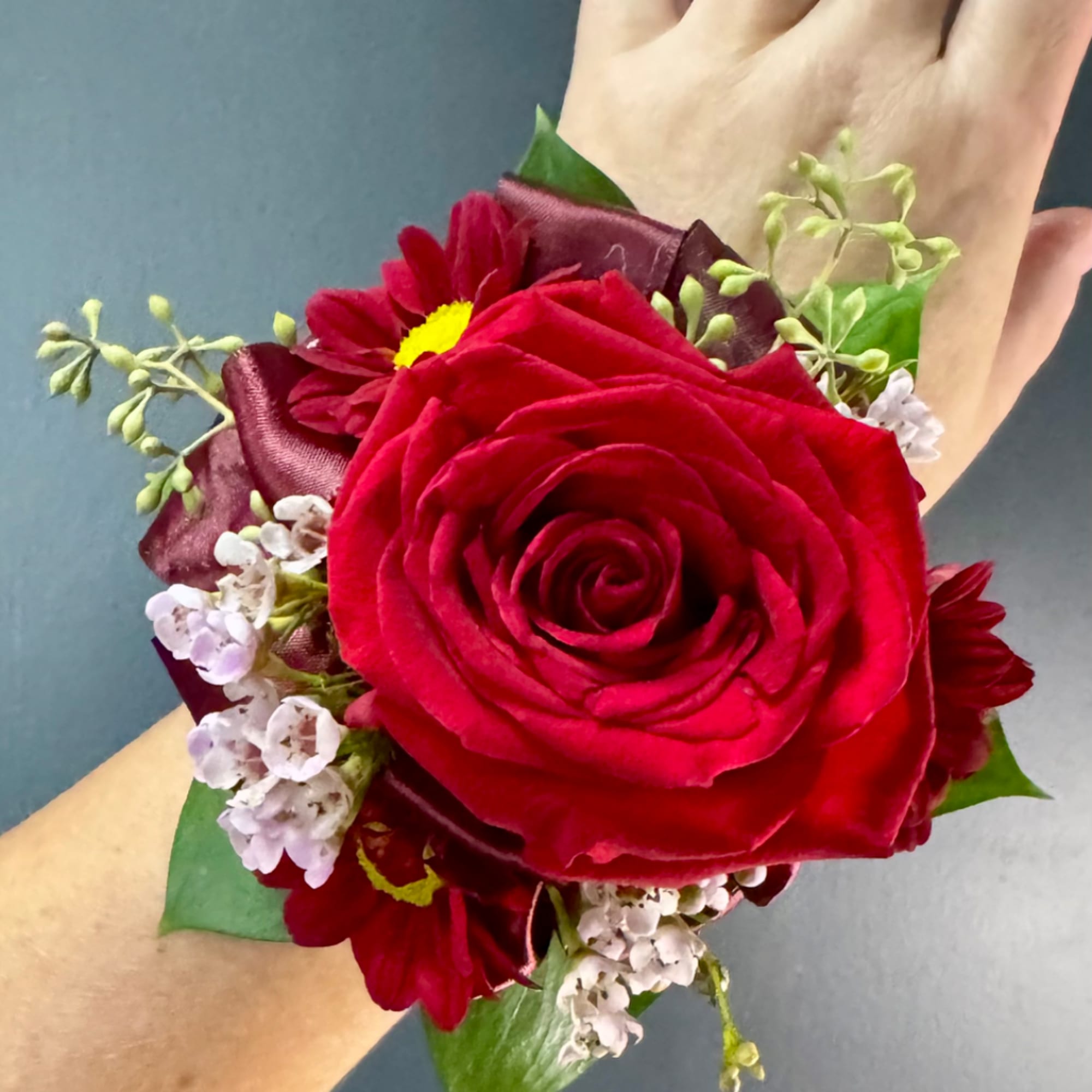Red rose wrist corsage with small white flowers and burgundy ribbon
