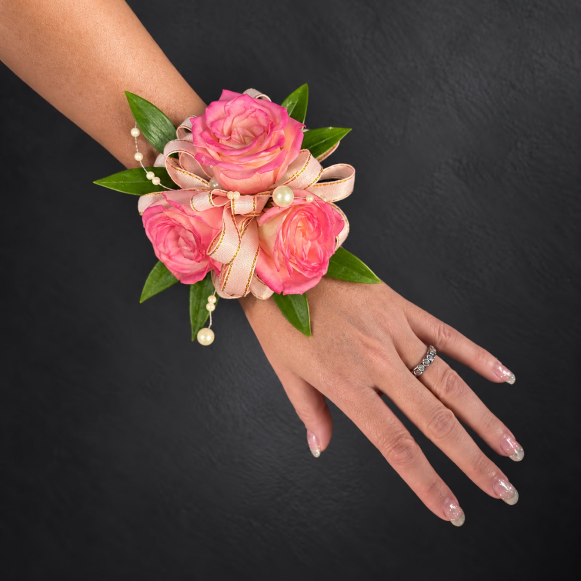 Pink rose wrist corsage with ribbon and pearl accents on a hand