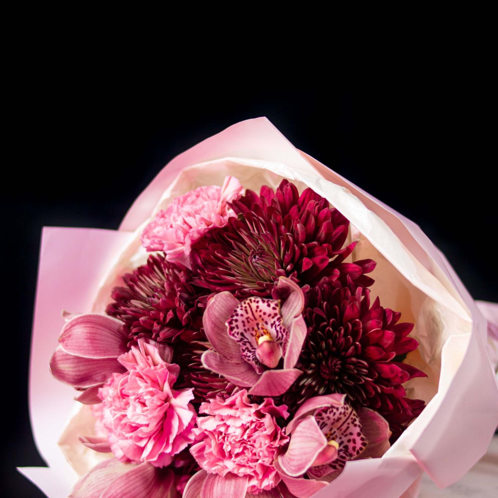 Deep burgundy blooms, soft blush carnations, and elegant orchids come together in