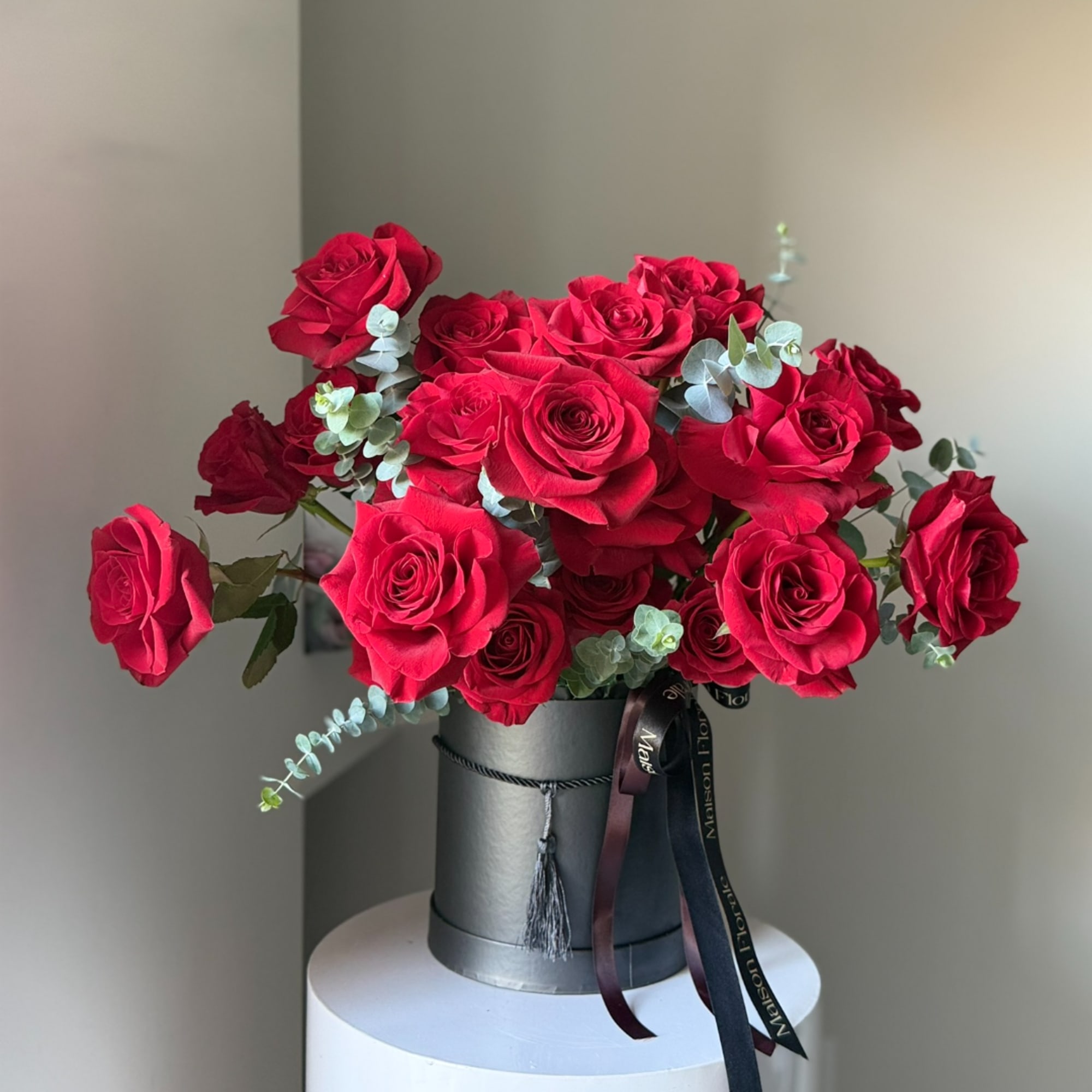Red roses arranged in a black hatbox with ribbon accents