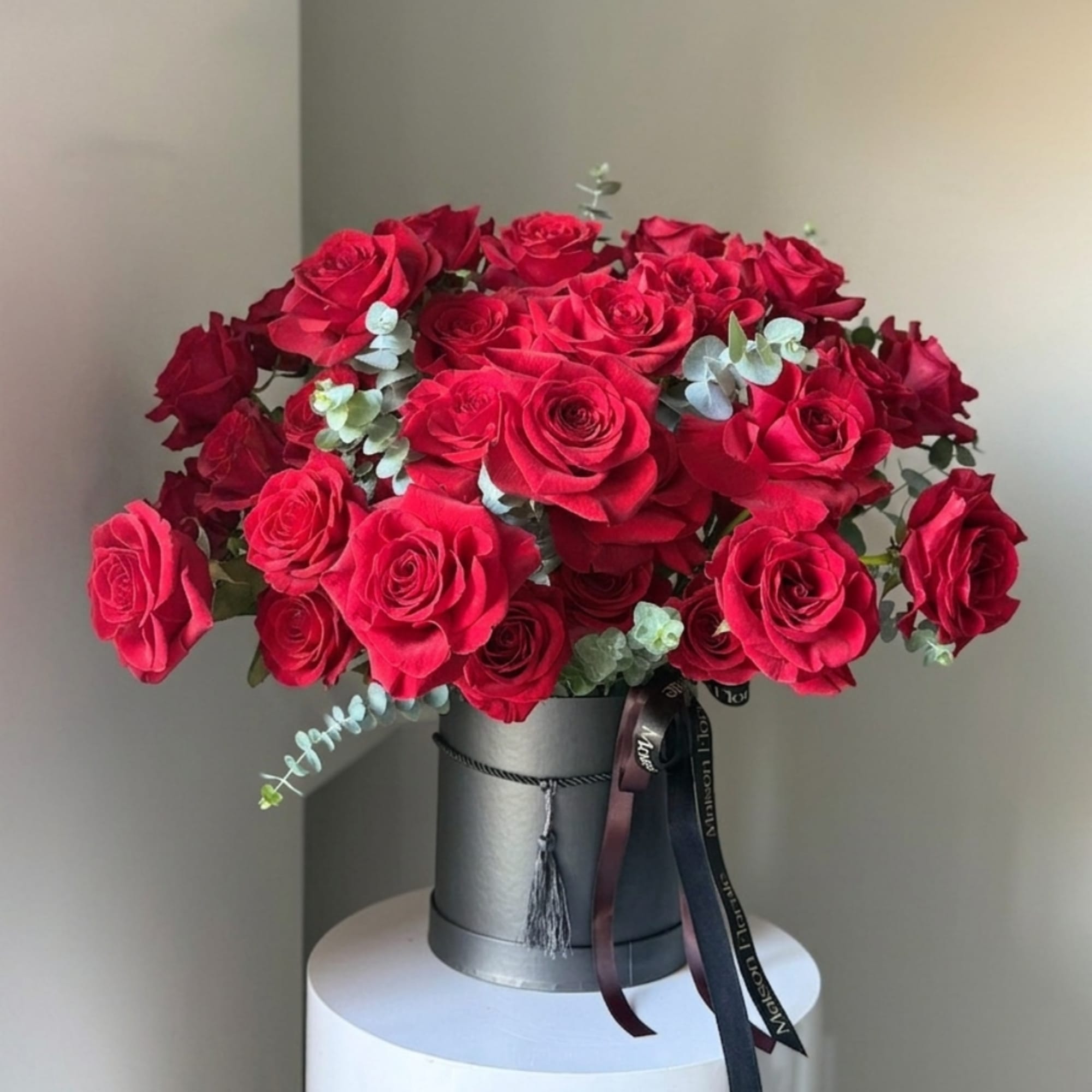 Red roses arranged in a gray hatbox with ribbon accents