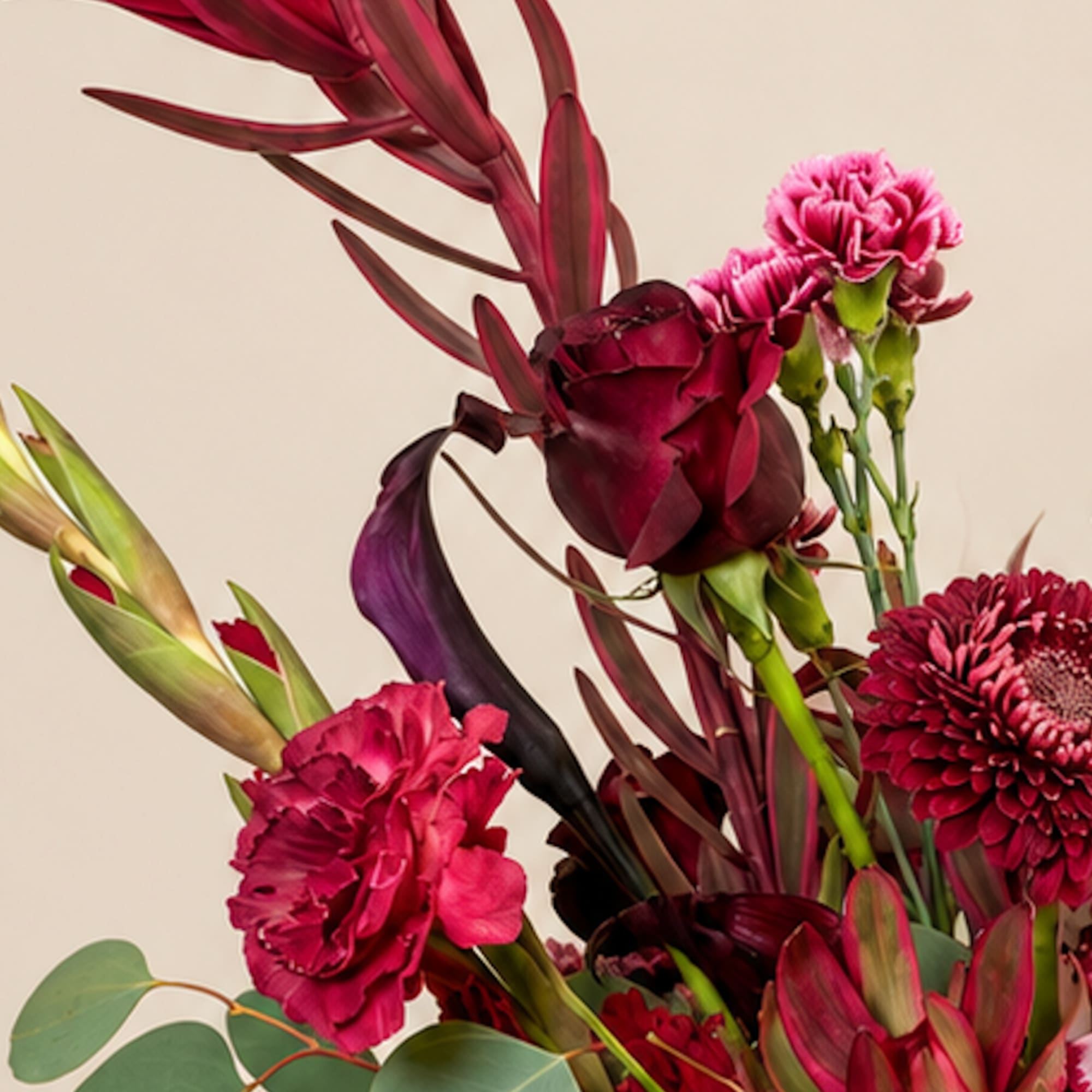 Deep pink and burgundy floral arrangement with tropical foliage against a neutral background