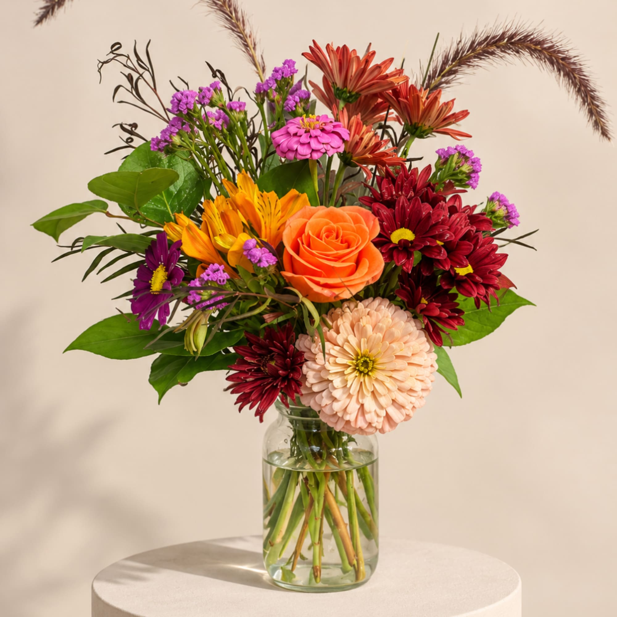 Mixed bouquet of orange, red, and pink flowers in a glass vase
