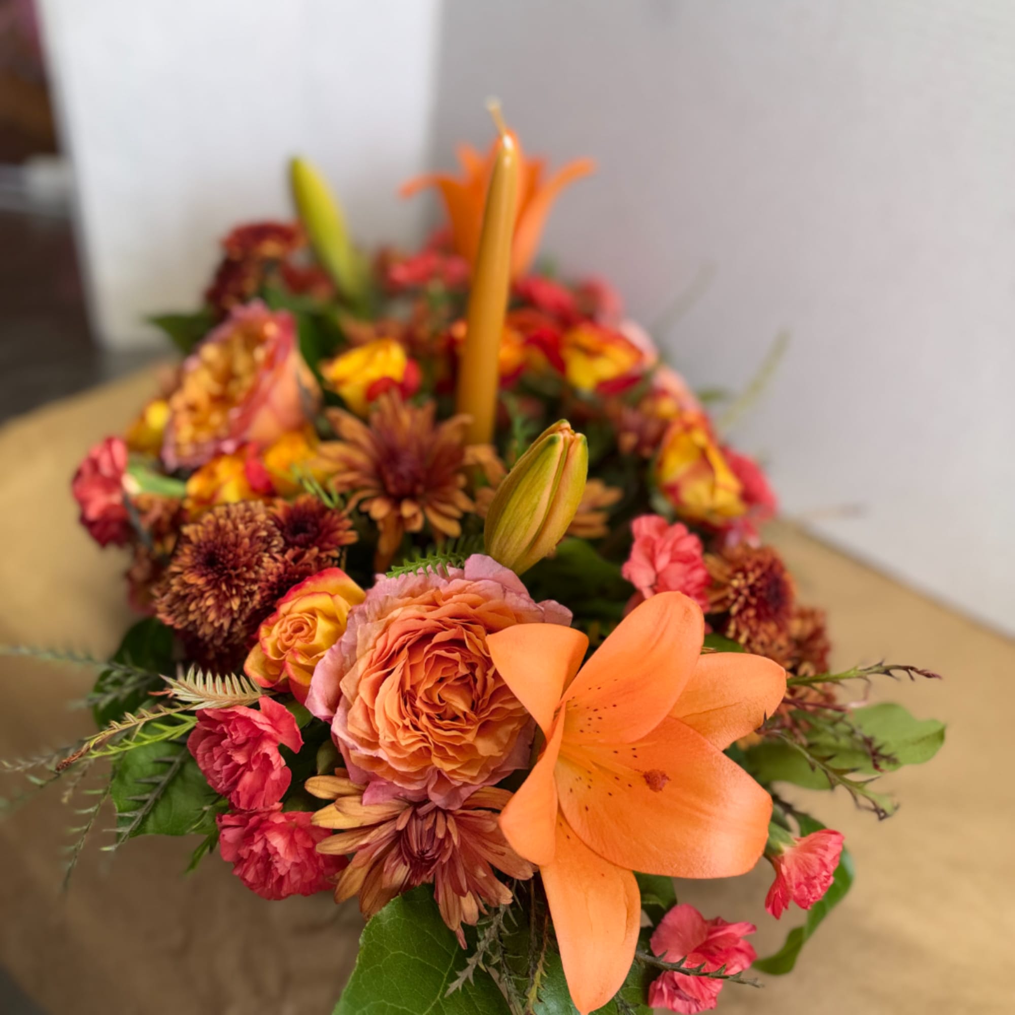 Orange lily and roses in a low floral centerpiece with candles