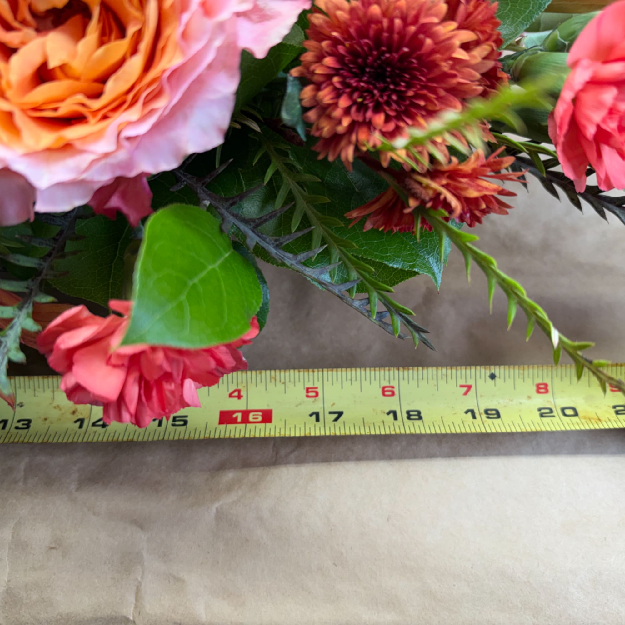 Close-up bouquet with pink and orange flowers beside a measuring tape