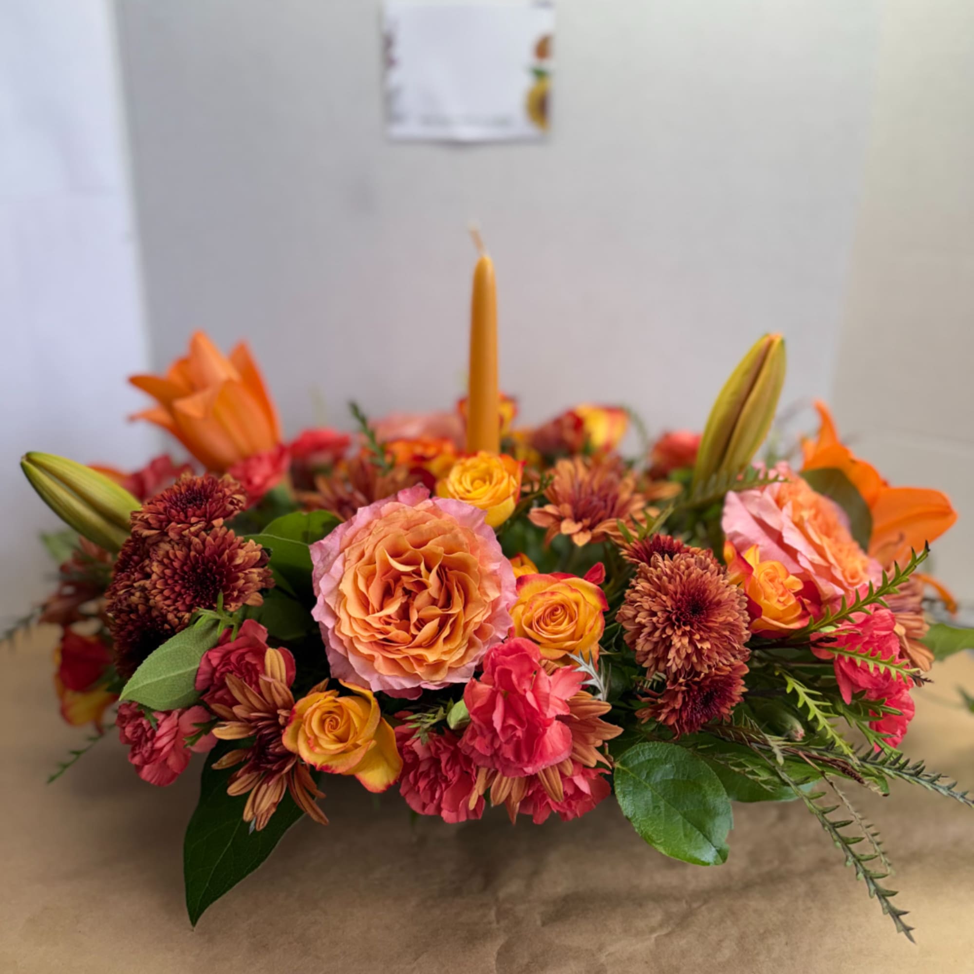 Low floral centerpiece with orange and pink blooms around a candle