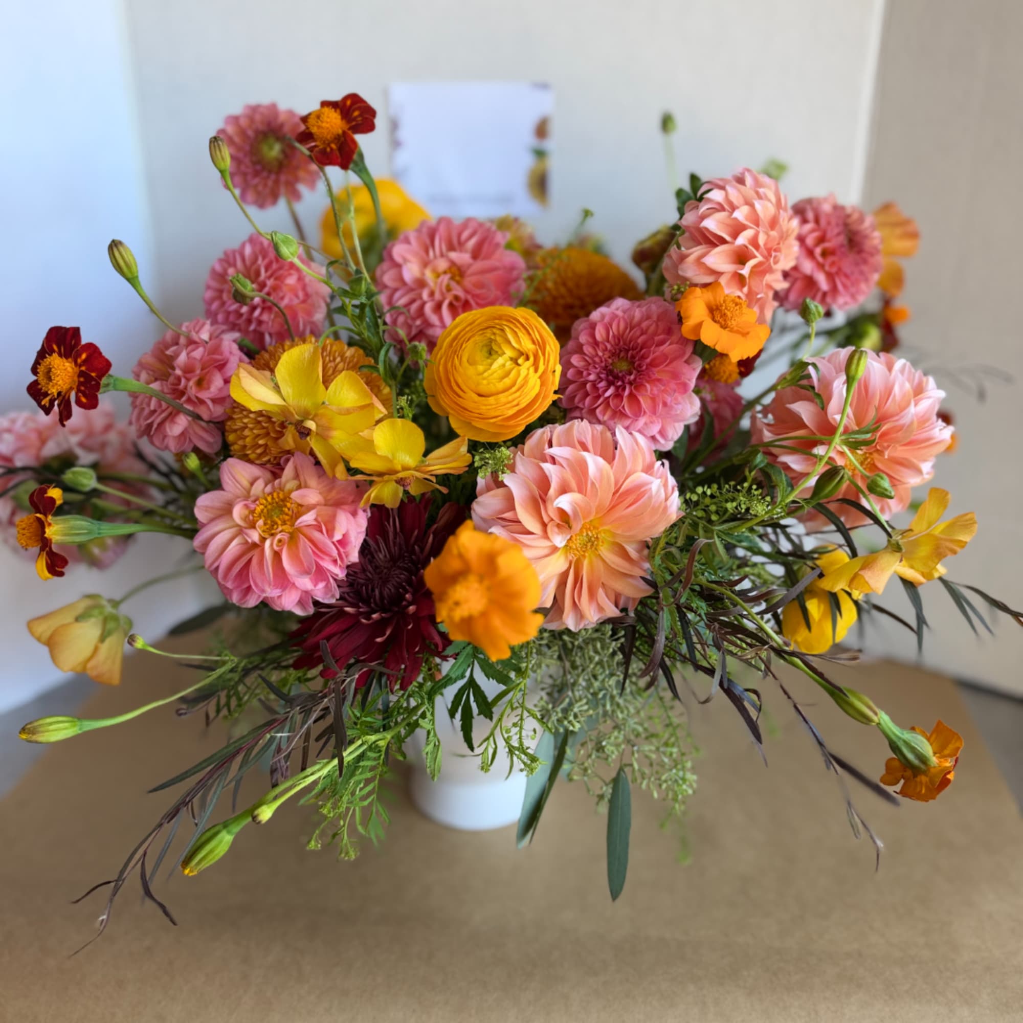Mixed bouquet of pink, peach, yellow, and orange flowers in a white vase