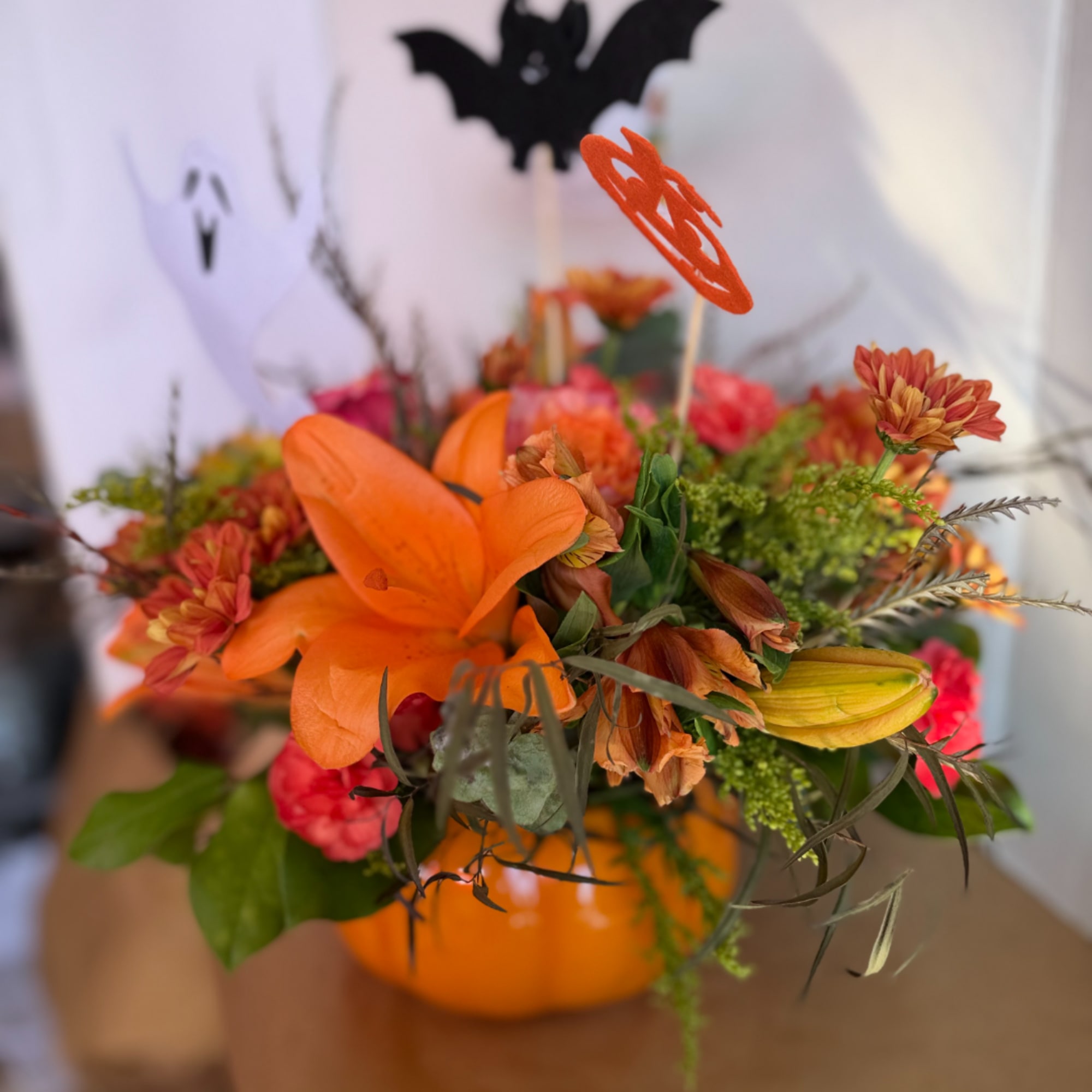 Orange floral arrangement in a pumpkin-shaped container with Halloween picks