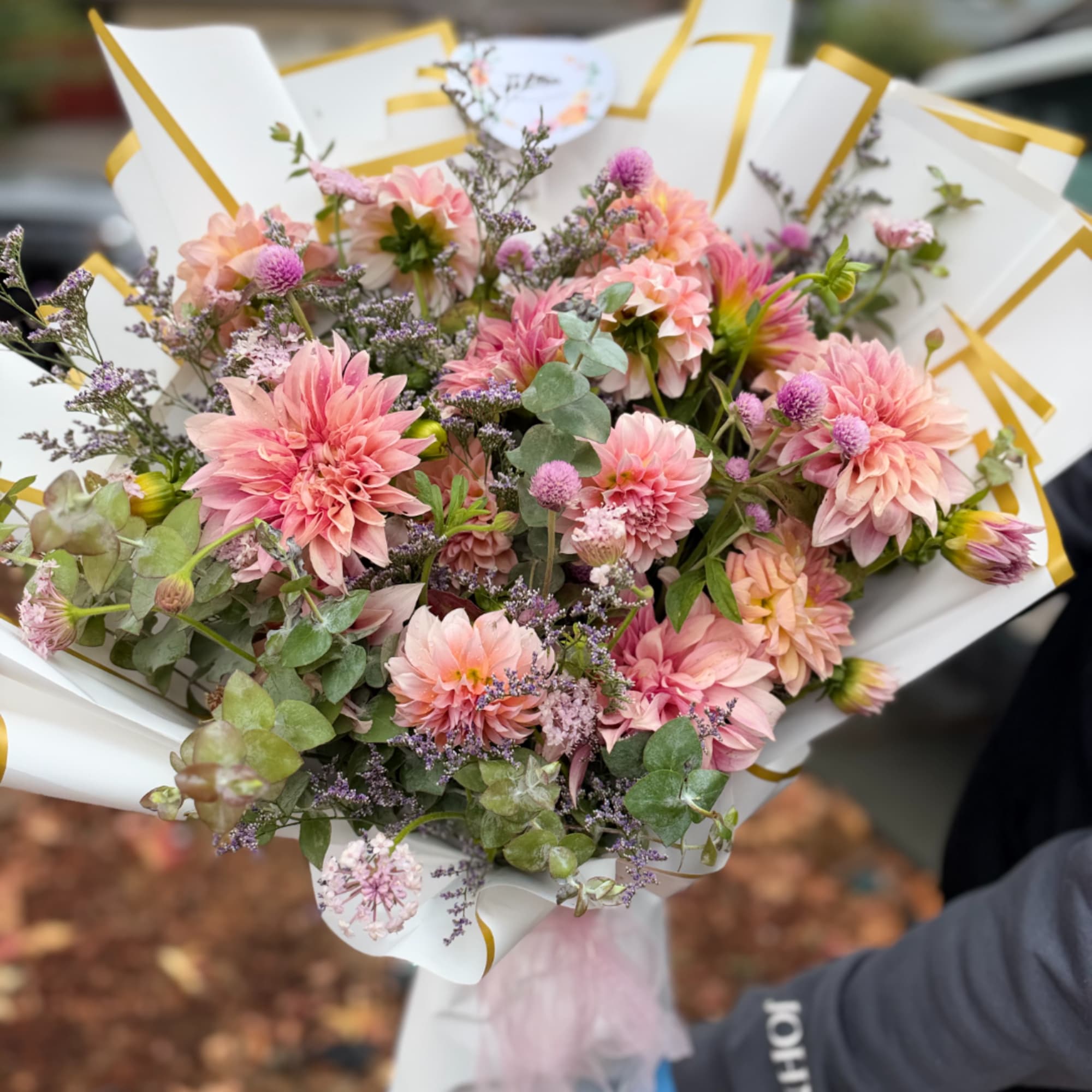 Bouquet of pink dahlias and purple filler flowers wrapped in white paper