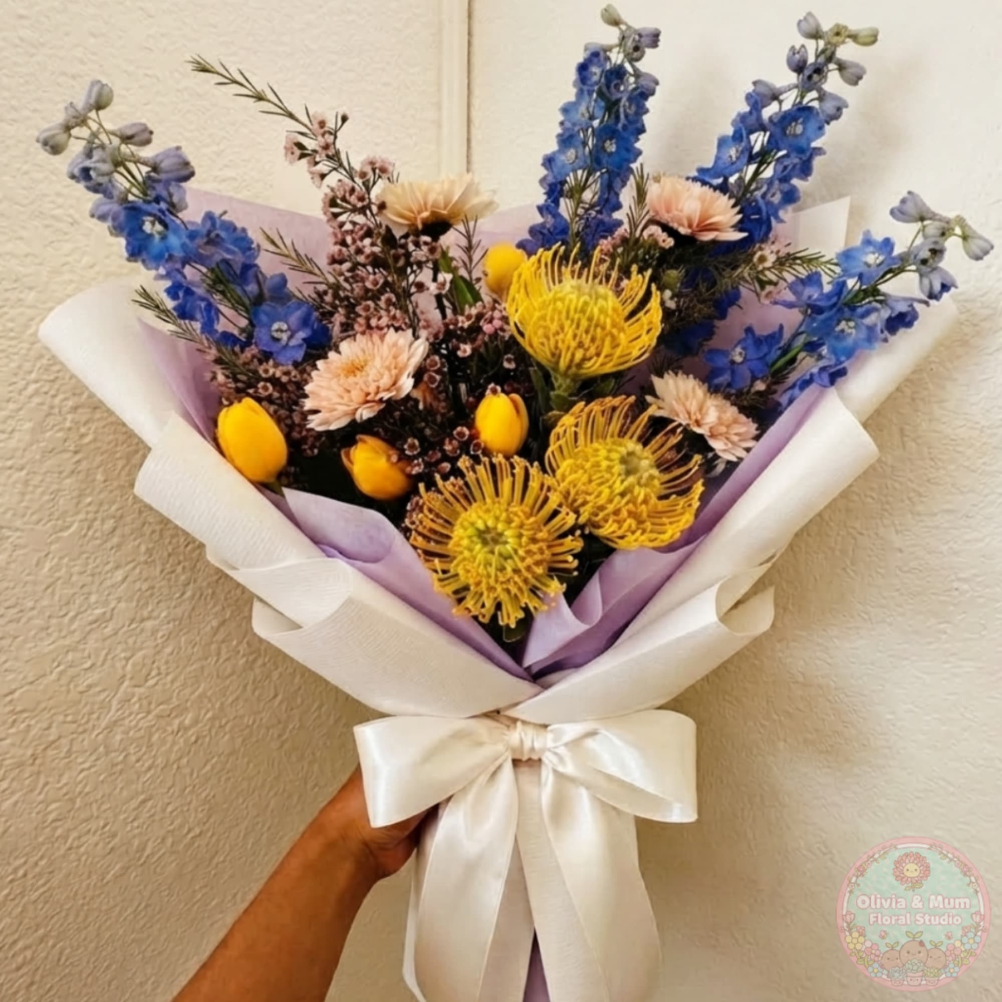 Hand-tied bouquet with blue, yellow, and pale pink flowers wrapped in white paper