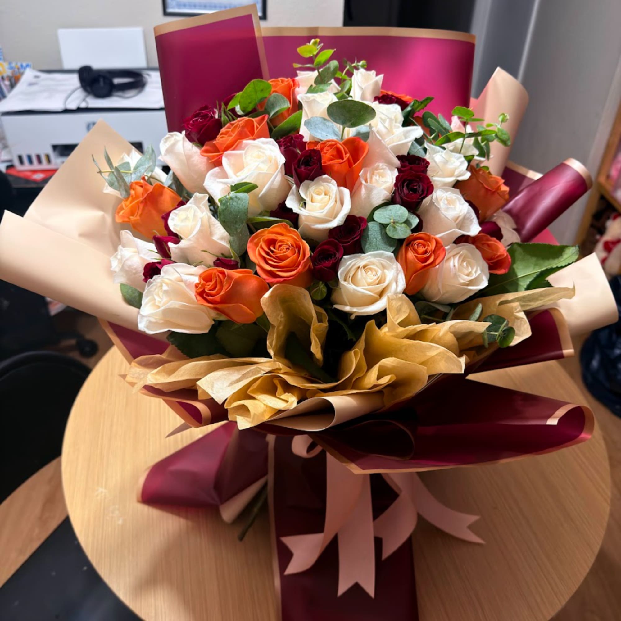 Bouquet of orange, white, and burgundy roses wrapped in burgundy paper