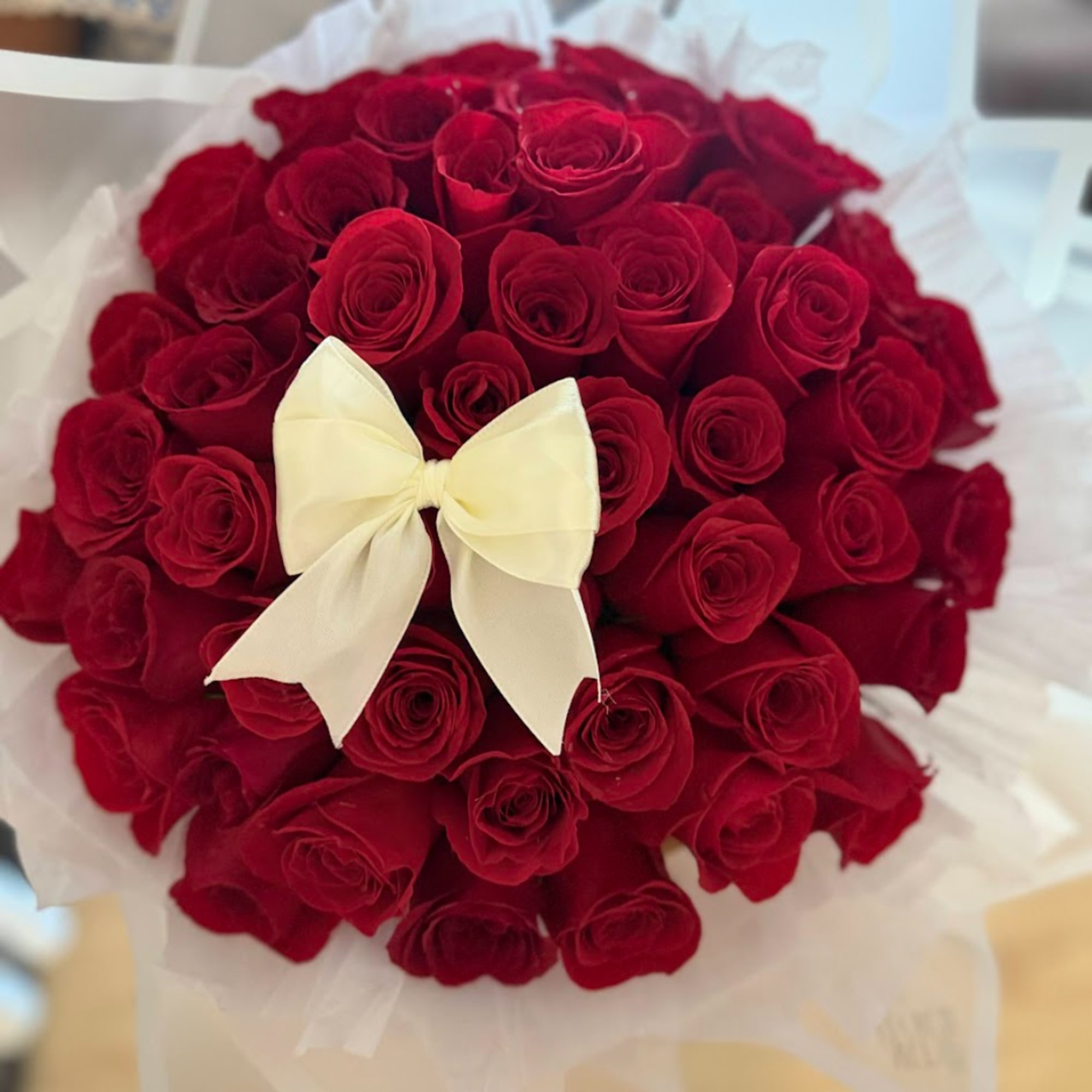 Round bouquet of red roses with a white bow and white wrapping