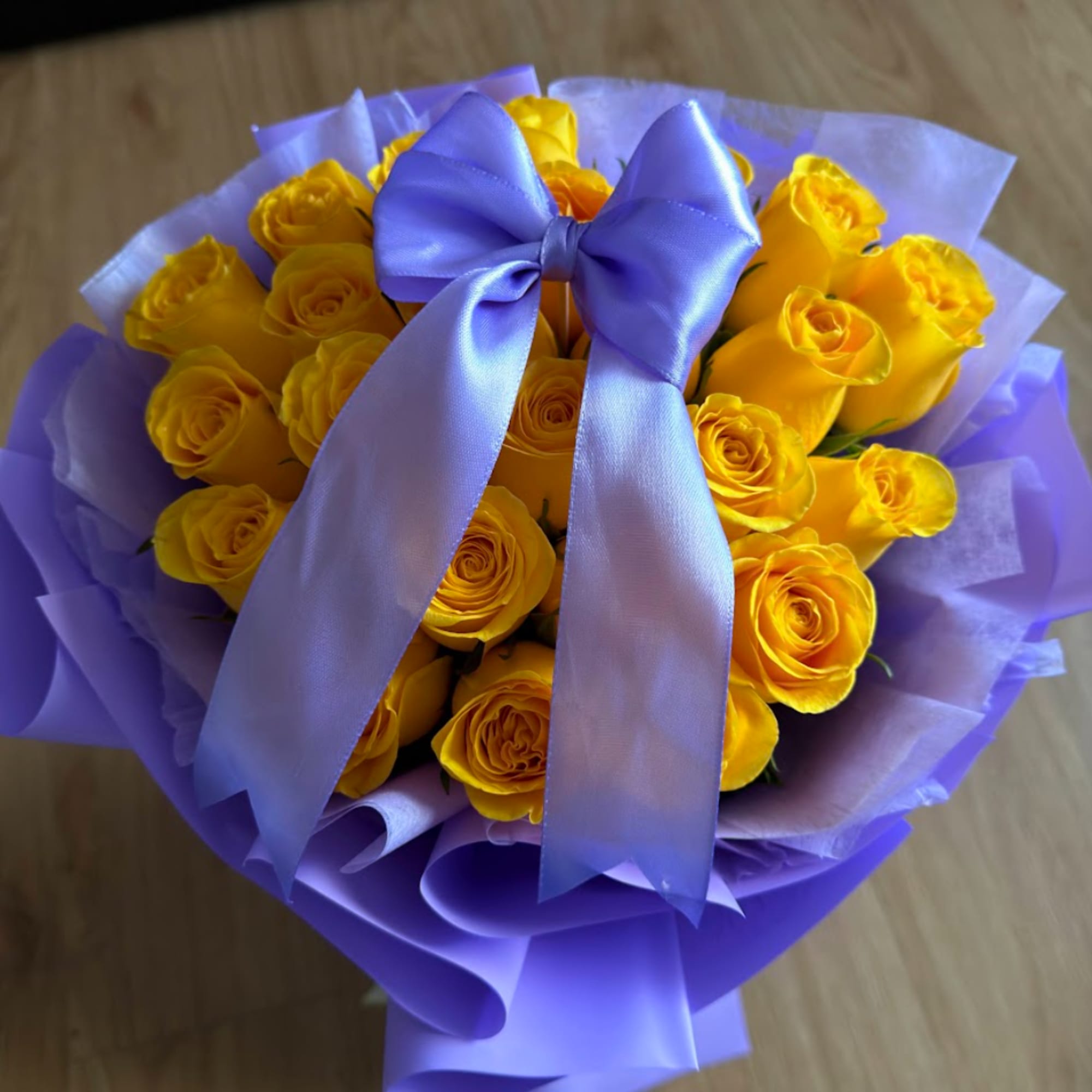 Bouquet of yellow roses wrapped in purple paper with a lavender ribbon