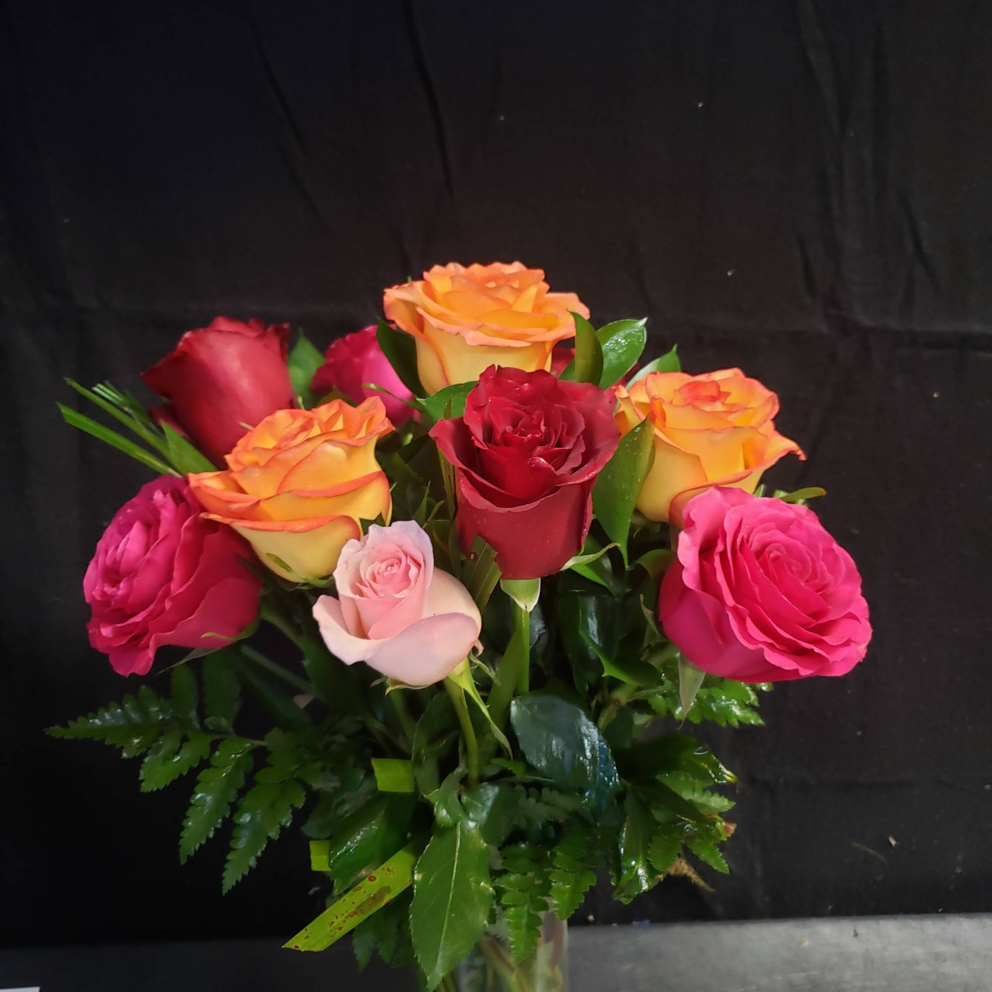 A compact cluster of roses in vivid pink, deep red, orange and