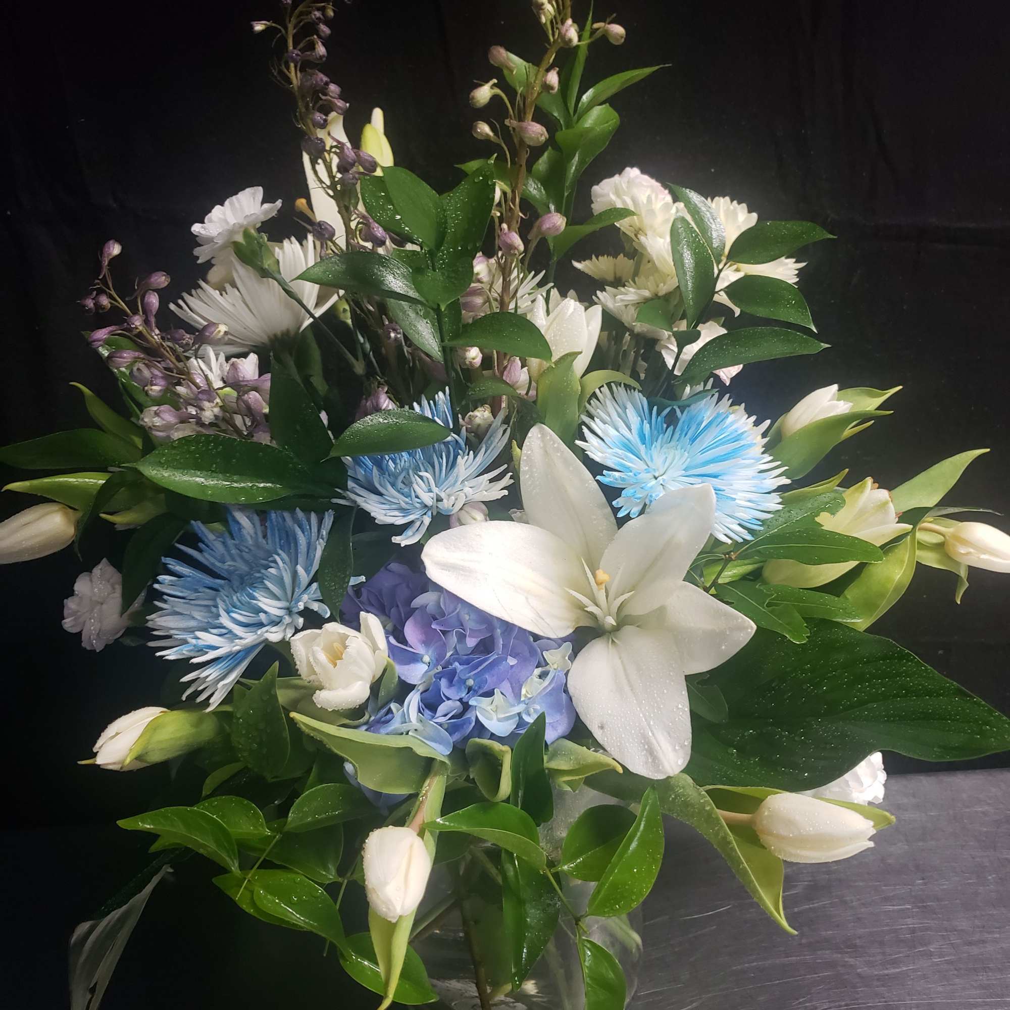 Large white lilies unfurl above a dense cluster of blue hydrangea and
