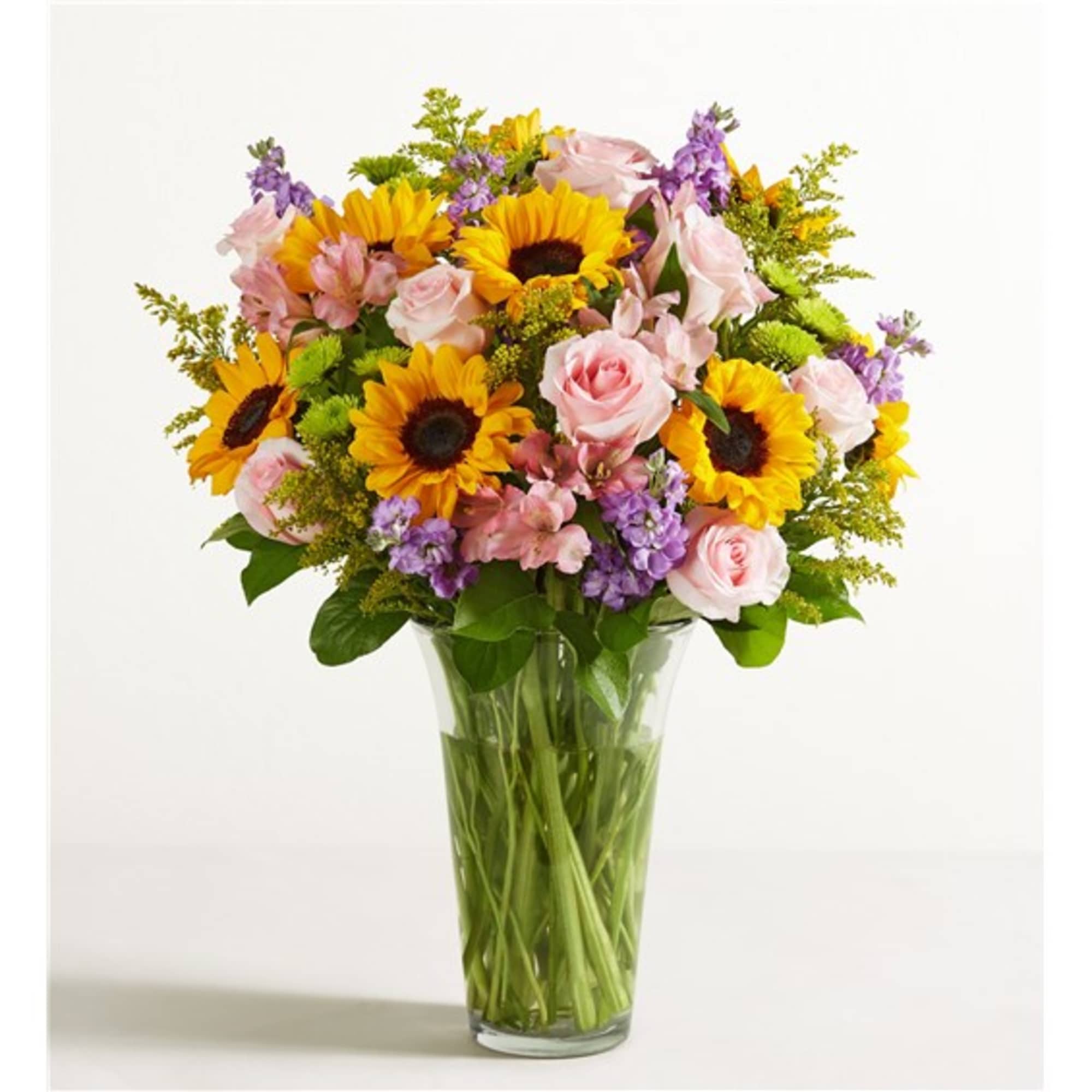 Bouquet of sunflowers, pink roses, and purple flowers in a clear glass vase