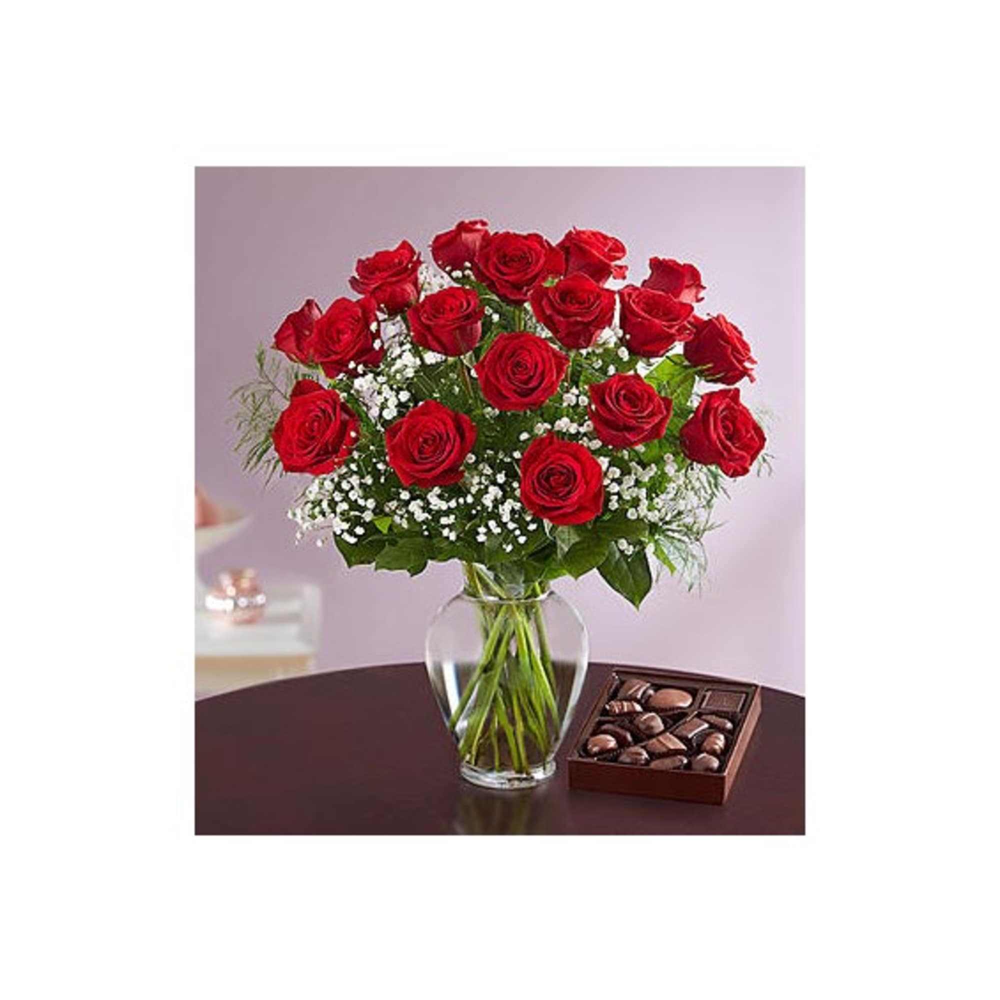 Red roses in a glass vase with a box of chocolates beside them