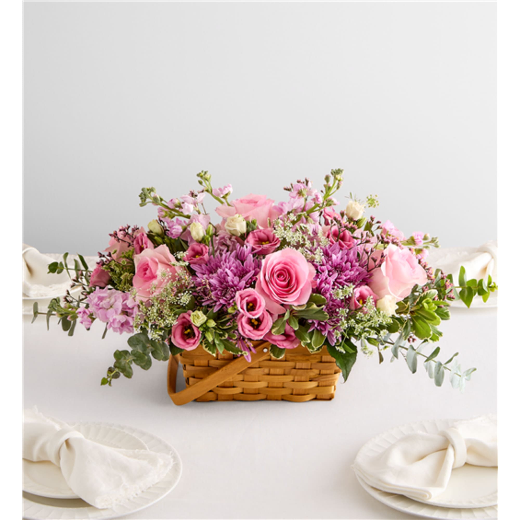 Pink and purple flower arrangement in a wicker basket on a white table