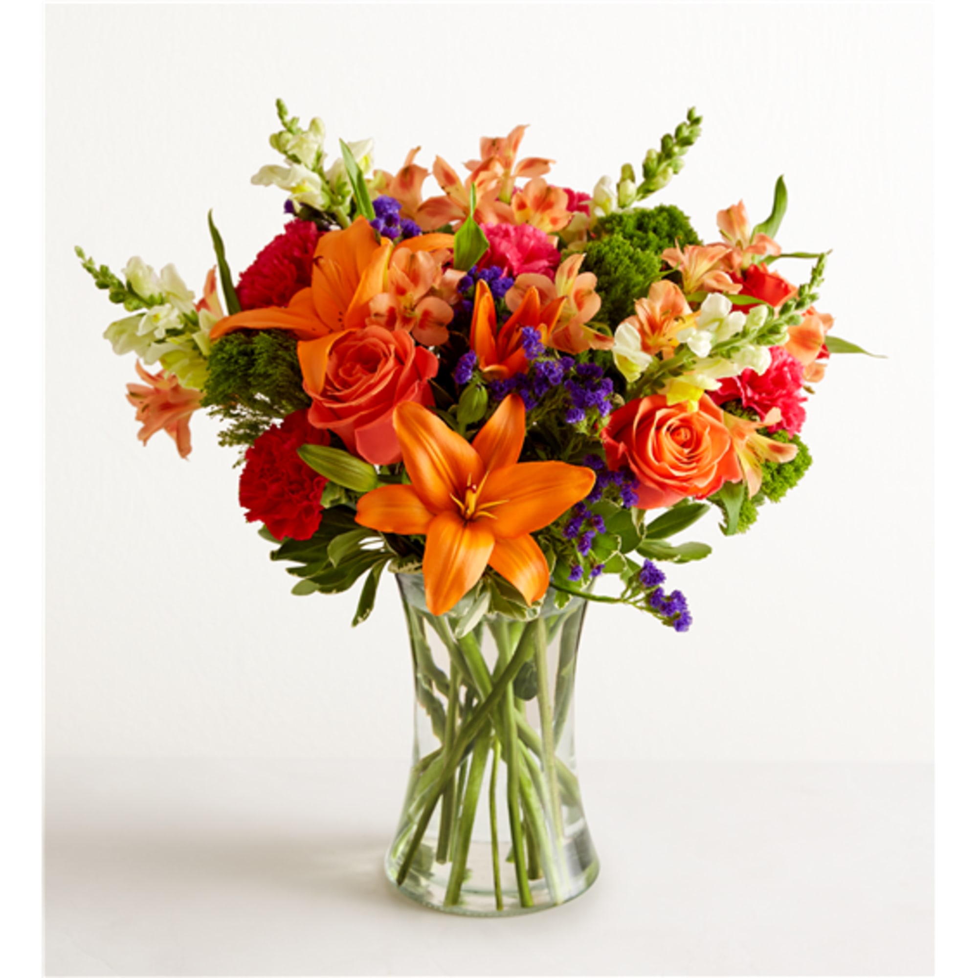 Bright mixed bouquet of orange, pink, and purple flowers in a clear glass vase